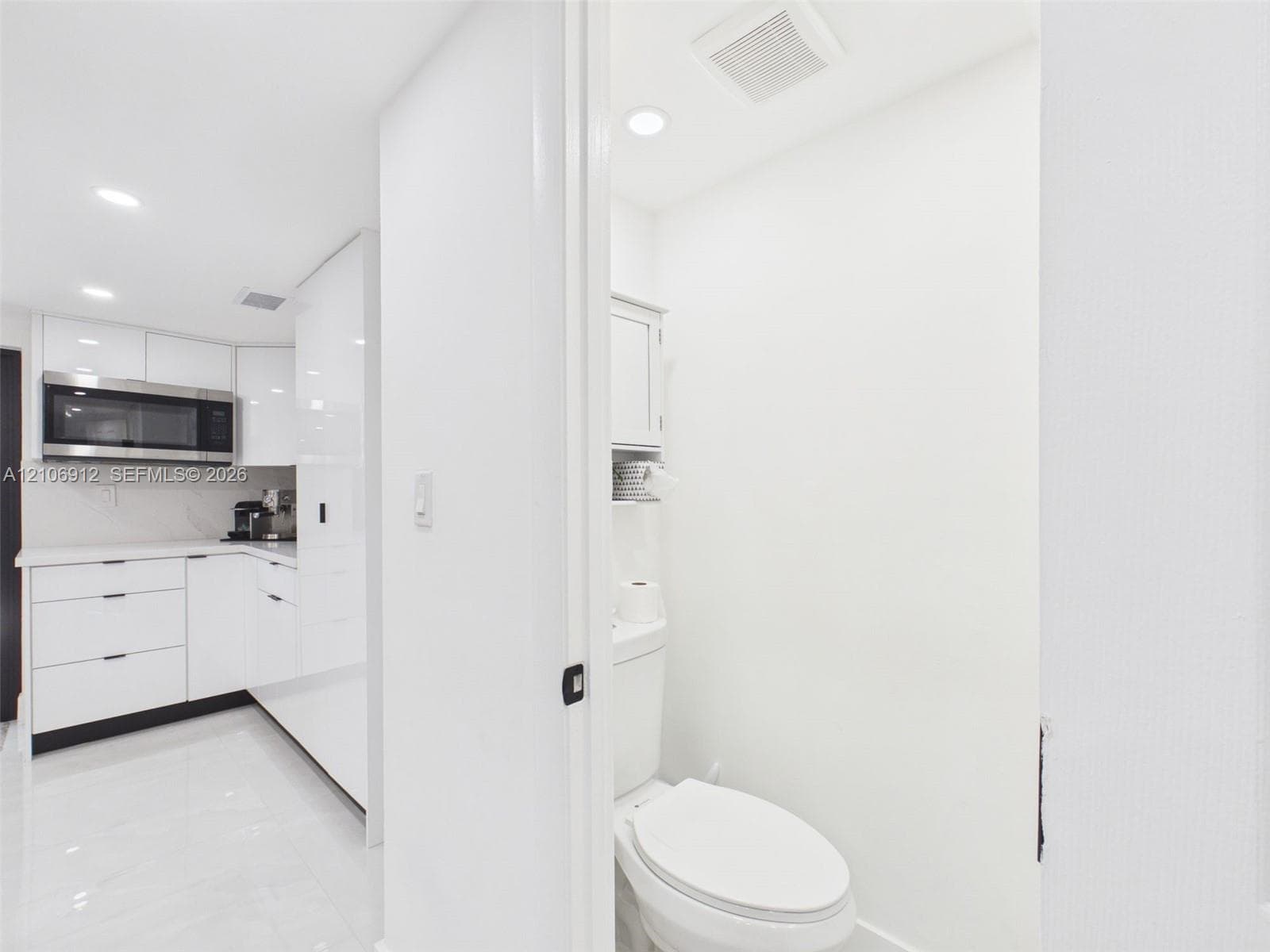 High-gloss cabinetry, stainless steel built-in microwave, stone countertops, recessed lighting, and tile flooring