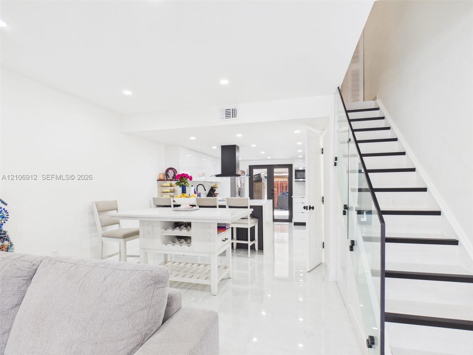 Staircase featuring glass paneling and dark-finished treads, high-gloss tile flooring, recessed ceiling lighting, and a kitchen area with a matte black range hood