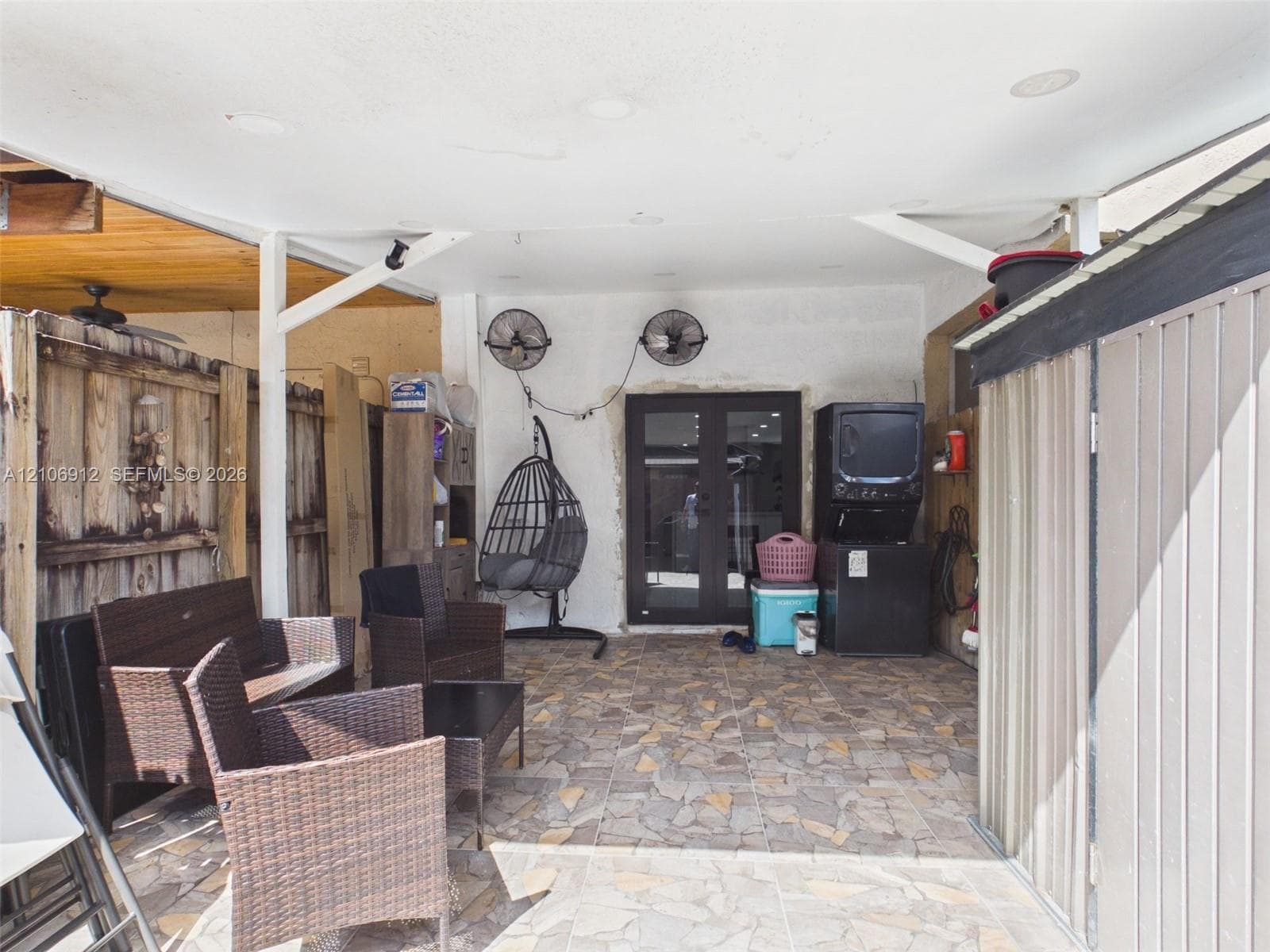 Covered patio featuring stone-tiled flooring, wall-mounted industrial fans, and a double-door entry