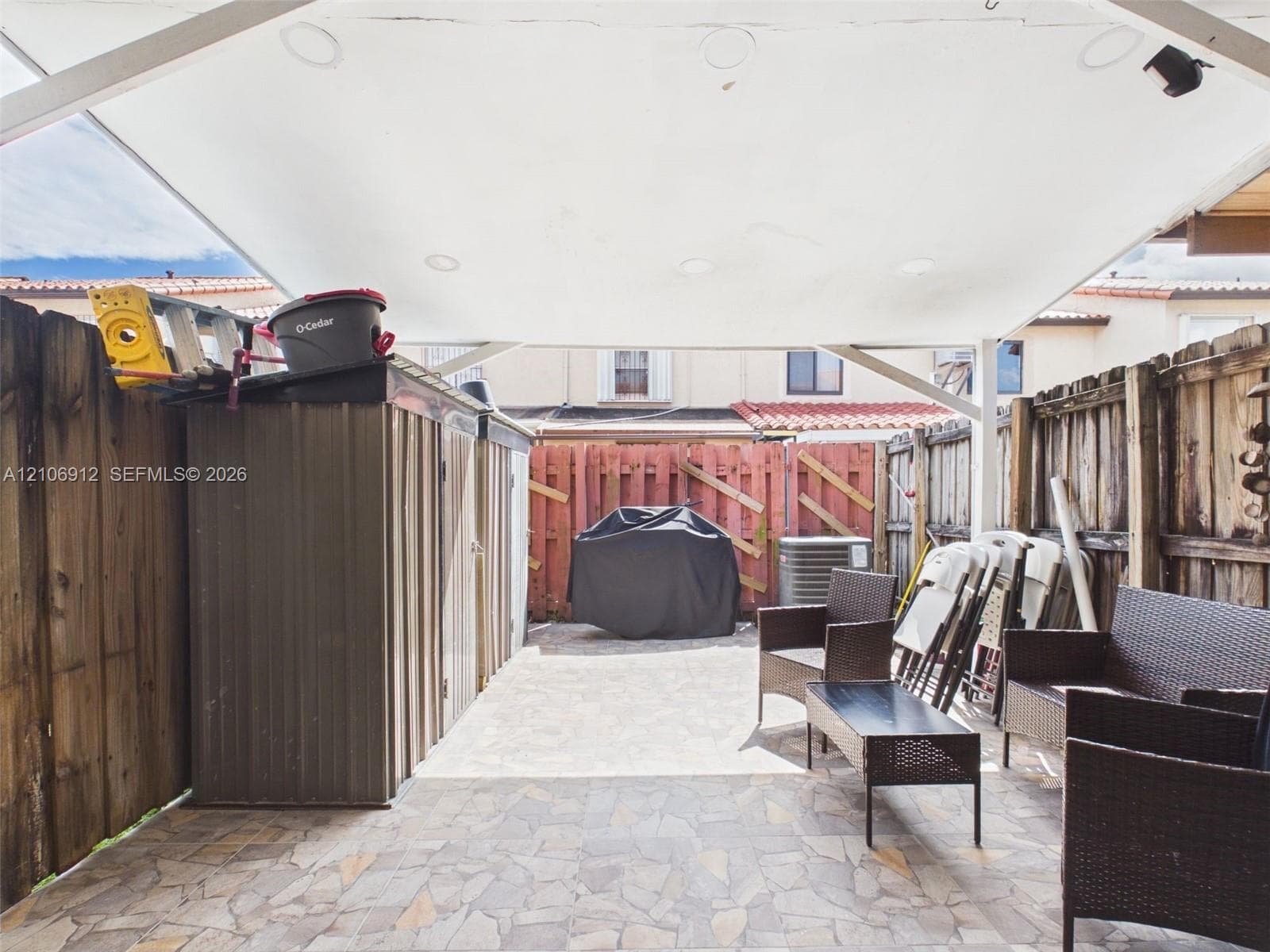 Covered patio featuring stone-tiled flooring, integrated recessed lighting, and enclosed wood fencing
