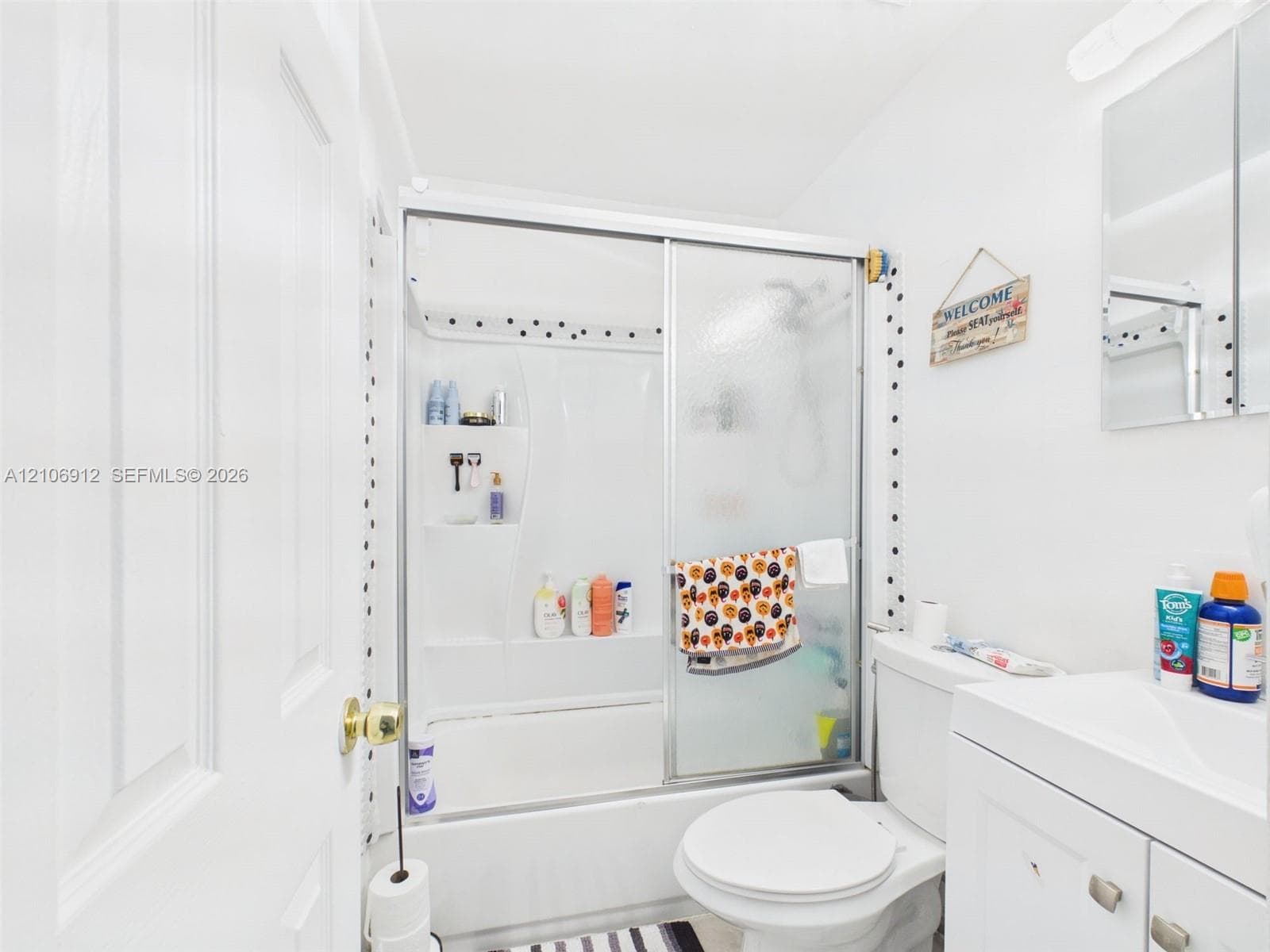 Bathroom featuring a shower and tub combination with sliding glass doors, a white vanity cabinet, and a mirrored medicine cabinet