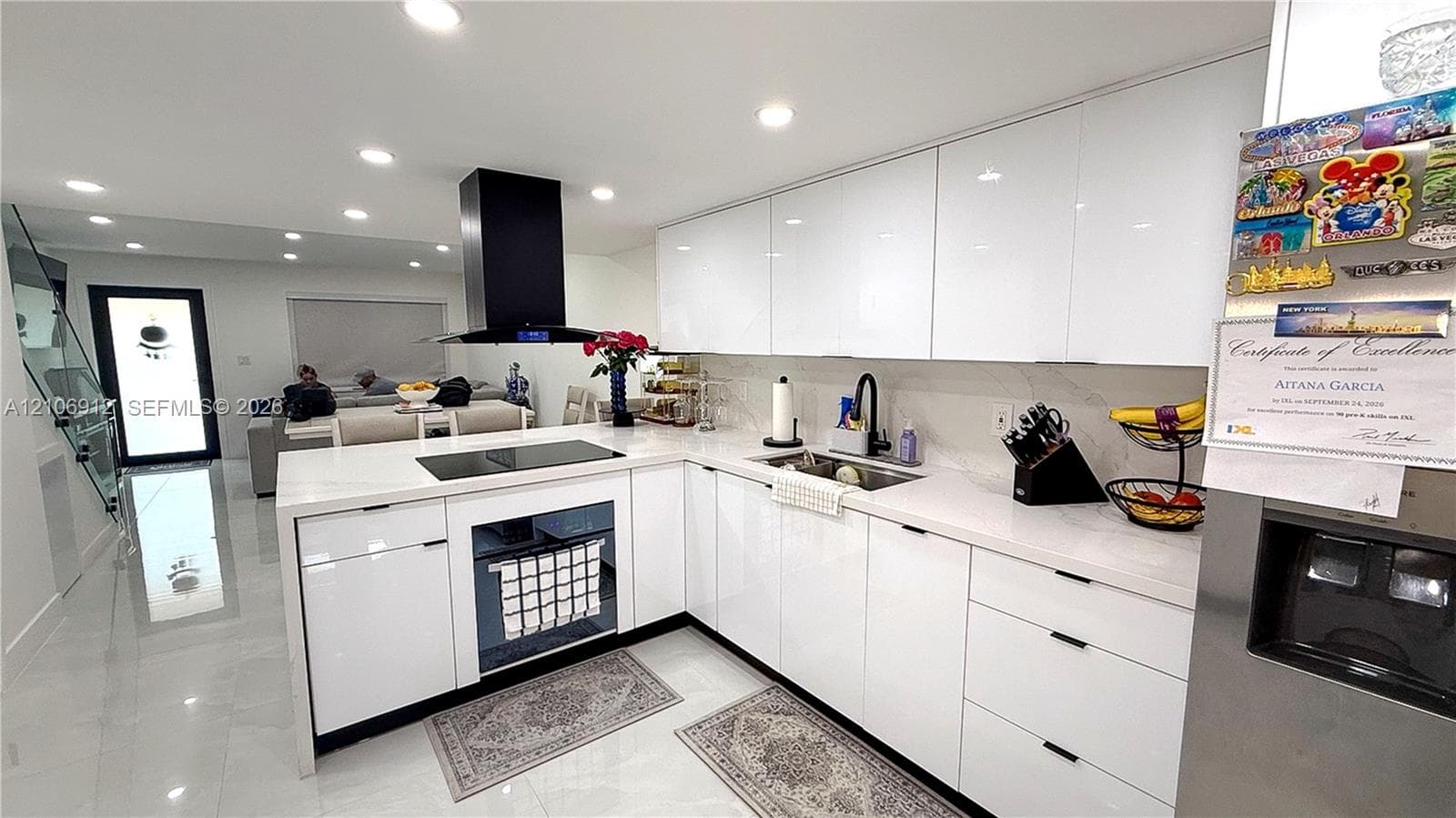 Kitchen featuring high-gloss cabinetry, stone countertops, a large island with an integrated cooktop, a contemporary black chimney-style range hood, and recessed lighting