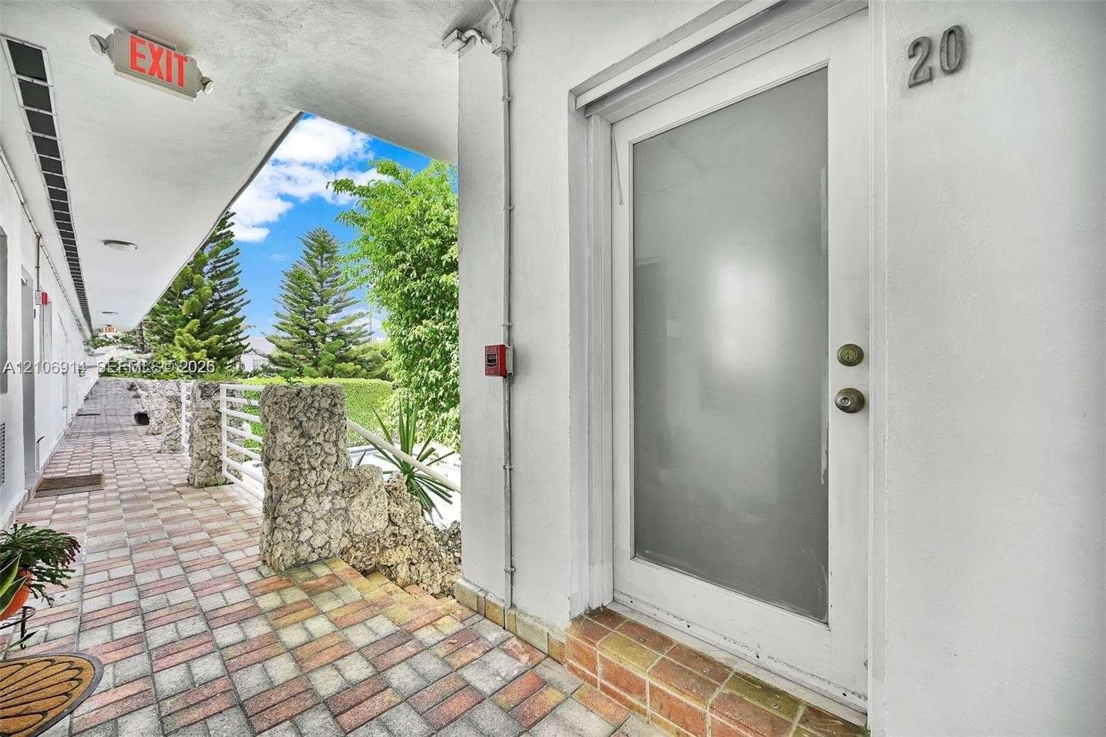 Exterior entrance featuring a frosted glass door, concrete block walkway, natural stone pillar accents, and a covered walkway