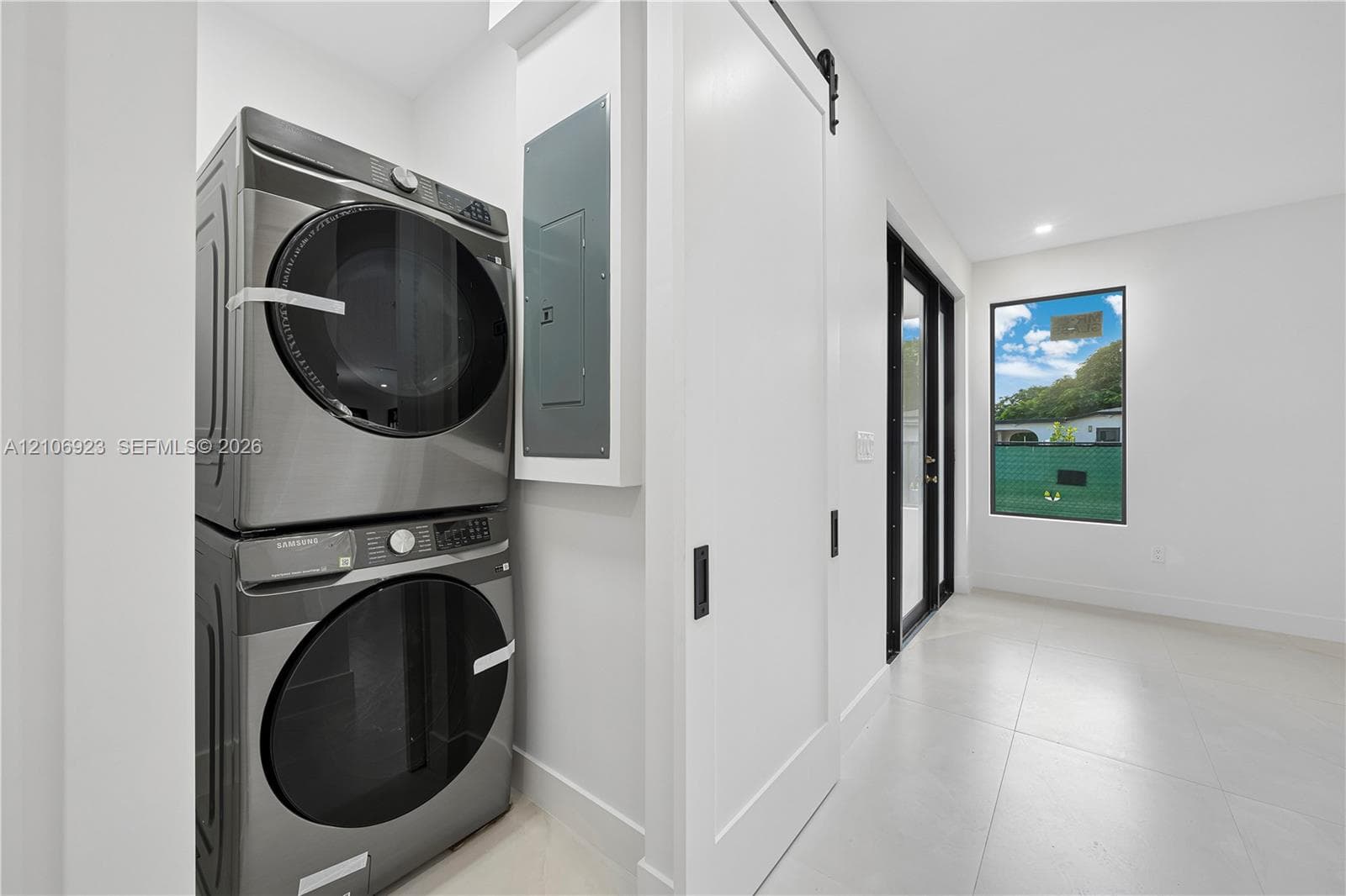 Laundry space featuring large-format tile flooring, a white sliding barn door with matte black hardware, and an exterior glass door with a black frame