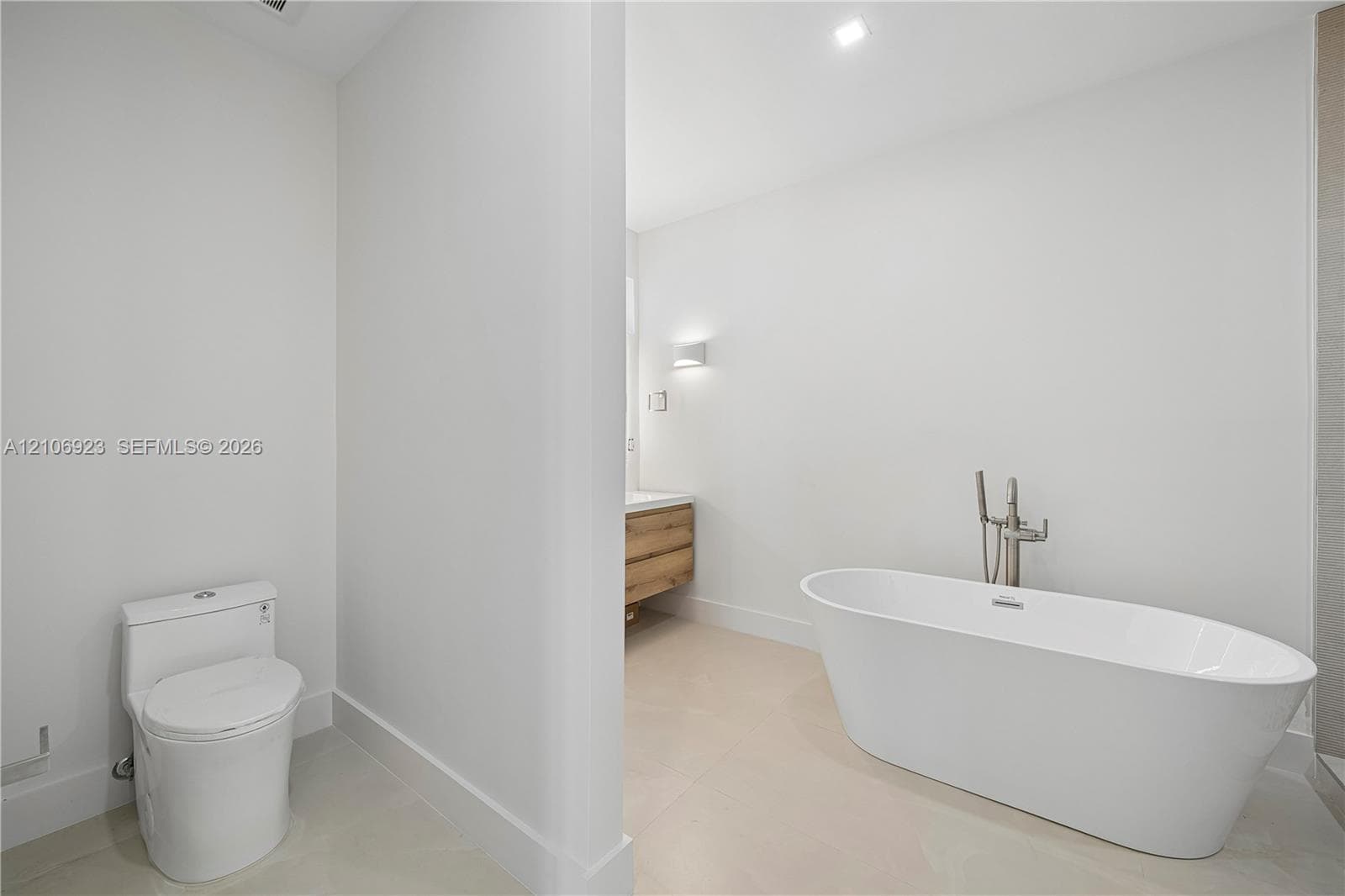 Freestanding white soaking tub with polished chrome floor-mounted faucet, wood-finish vanity with countertop basin, and low-profile elongated toilet
