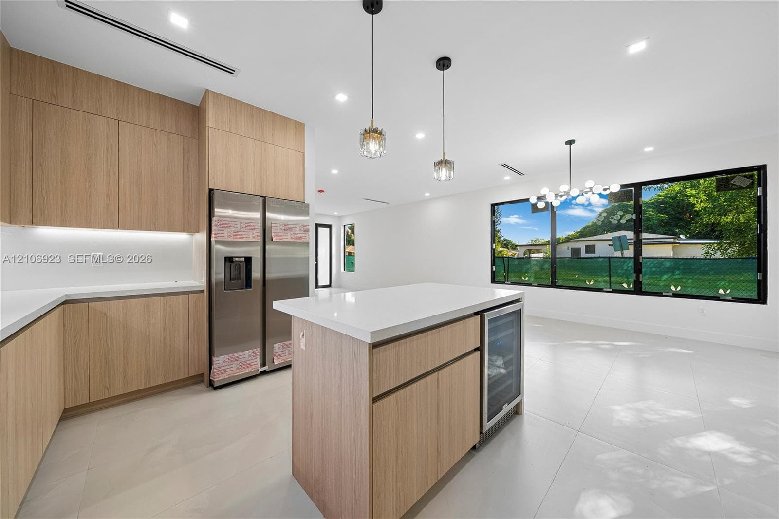 Kitchen featuring wood-finish flat-panel cabinetry, quartz countertops, a central island with an integrated wine cooler, stainless steel refrigerator, and large picture windows