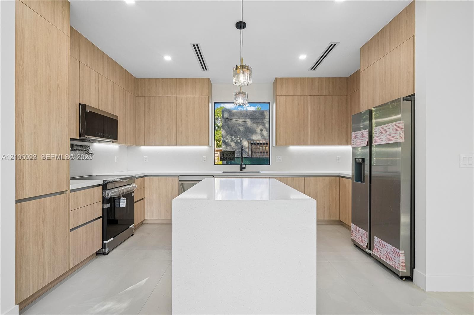 Modern kitchen featuring flat-panel wood-finish cabinetry, a large quartz-topped island, stainless steel appliances, under-cabinet lighting, and recessed ceiling lighting