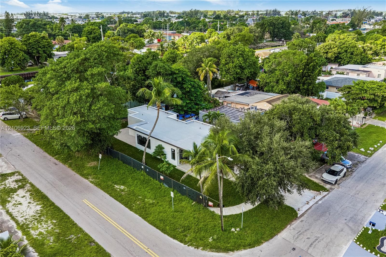 Single-story residence featuring a flat roofline, corner lot placement, mature landscaping, palm trees, and an asphalt driveway