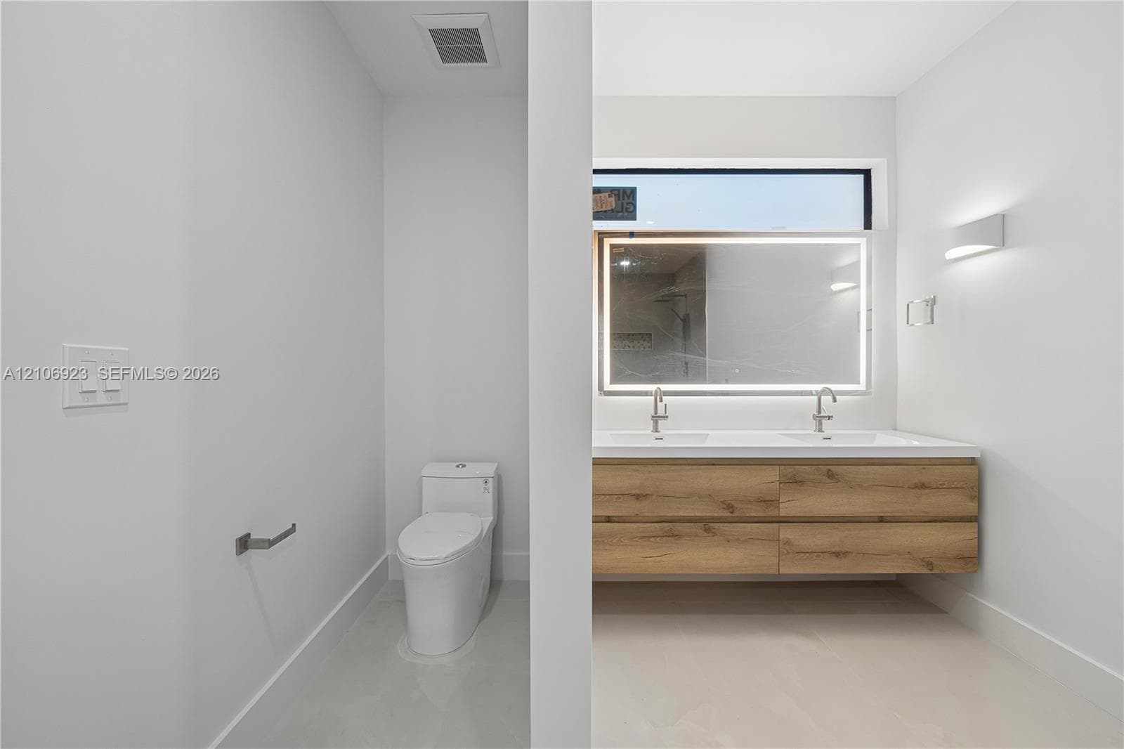 Dual-sink floating vanity with wood-finish cabinetry, rectangular vessel sinks, wall-mounted faucets, and an integrated LED-backlit mirror featuring a horizontal clerestory window