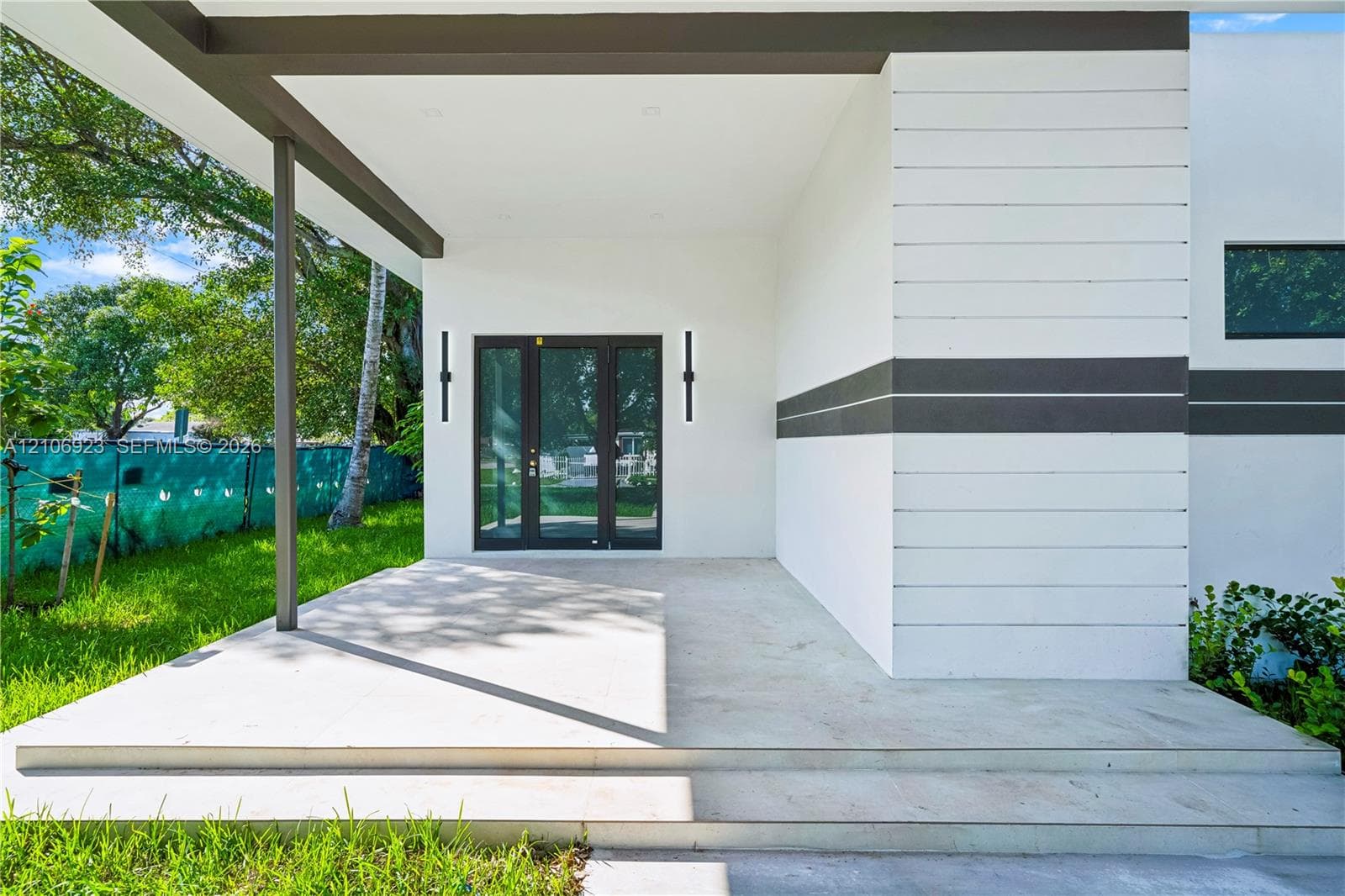 Modern entrance featuring horizontal wood-panel siding, a covered concrete porch, tiered stairs, and dual vertical wall-mounted exterior light fixtures