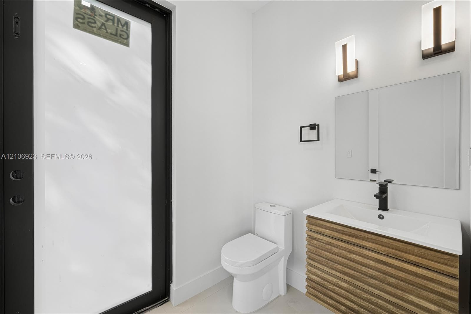 Floating vanity featuring wood-finish reeded detailing, white integrated countertop, matte black faucet, wall-mounted rectangular mirror, and dual vertical sconces