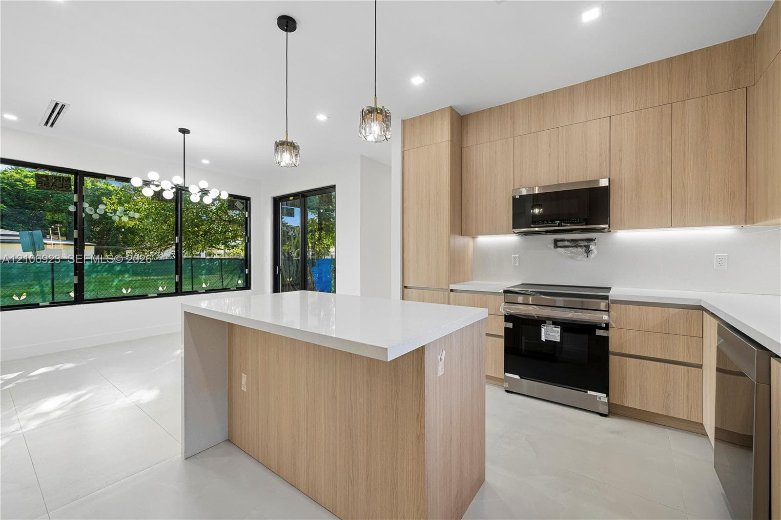 Kitchen featuring light wood-finish cabinetry, a central island with a white countertop, large-format tile flooring, stainless steel appliances, and integrated under-cabinet lighting