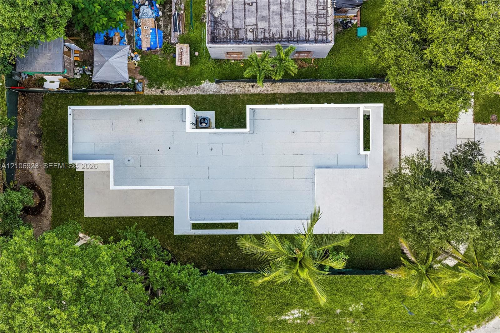 Aerial perspective of property featuring a flat roofline, concrete driveway, and established trees within the lot boundaries