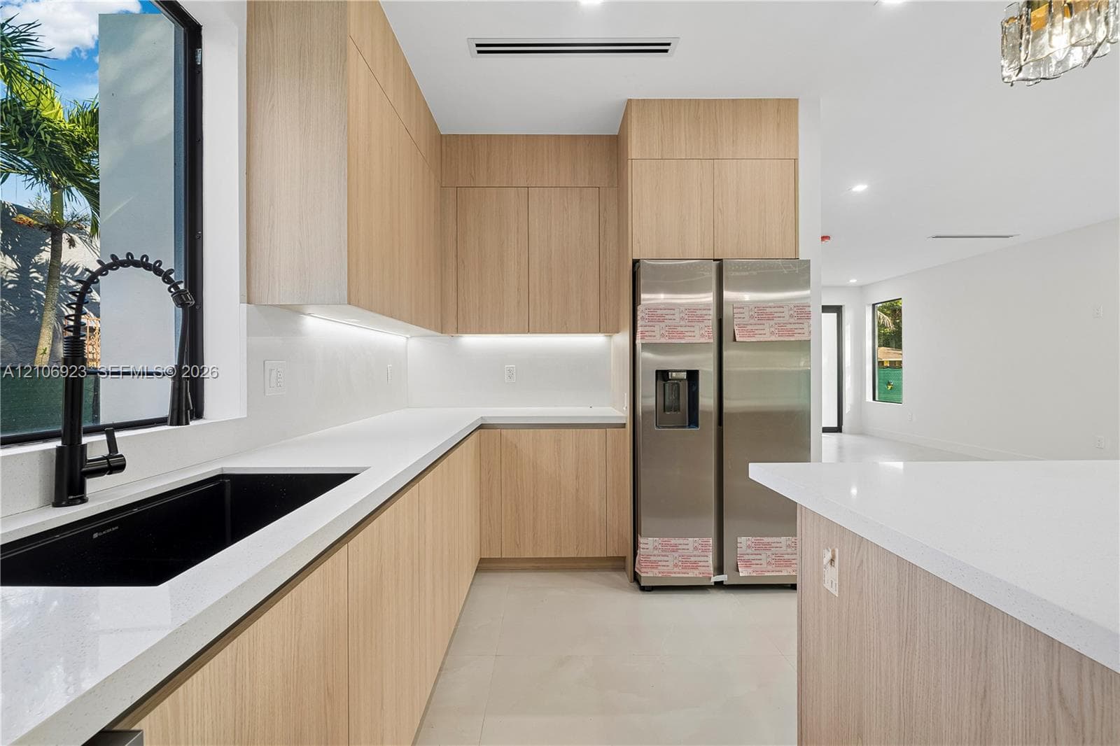 Kitchen featuring flat-panel wood-finish cabinetry, white countertops, black undermount sink with high-arc faucet, stainless steel refrigerator, and recessed lighting