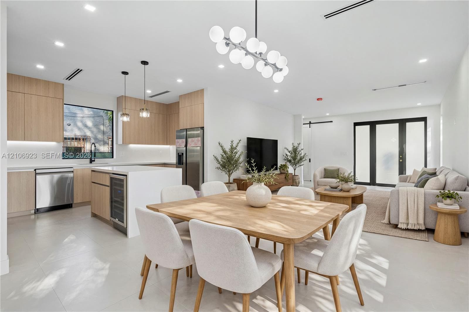 Open-concept kitchen featuring light wood-finish cabinetry, a central island with an integrated beverage cooler, stainless steel appliances, and a modern multi-globe chandelier