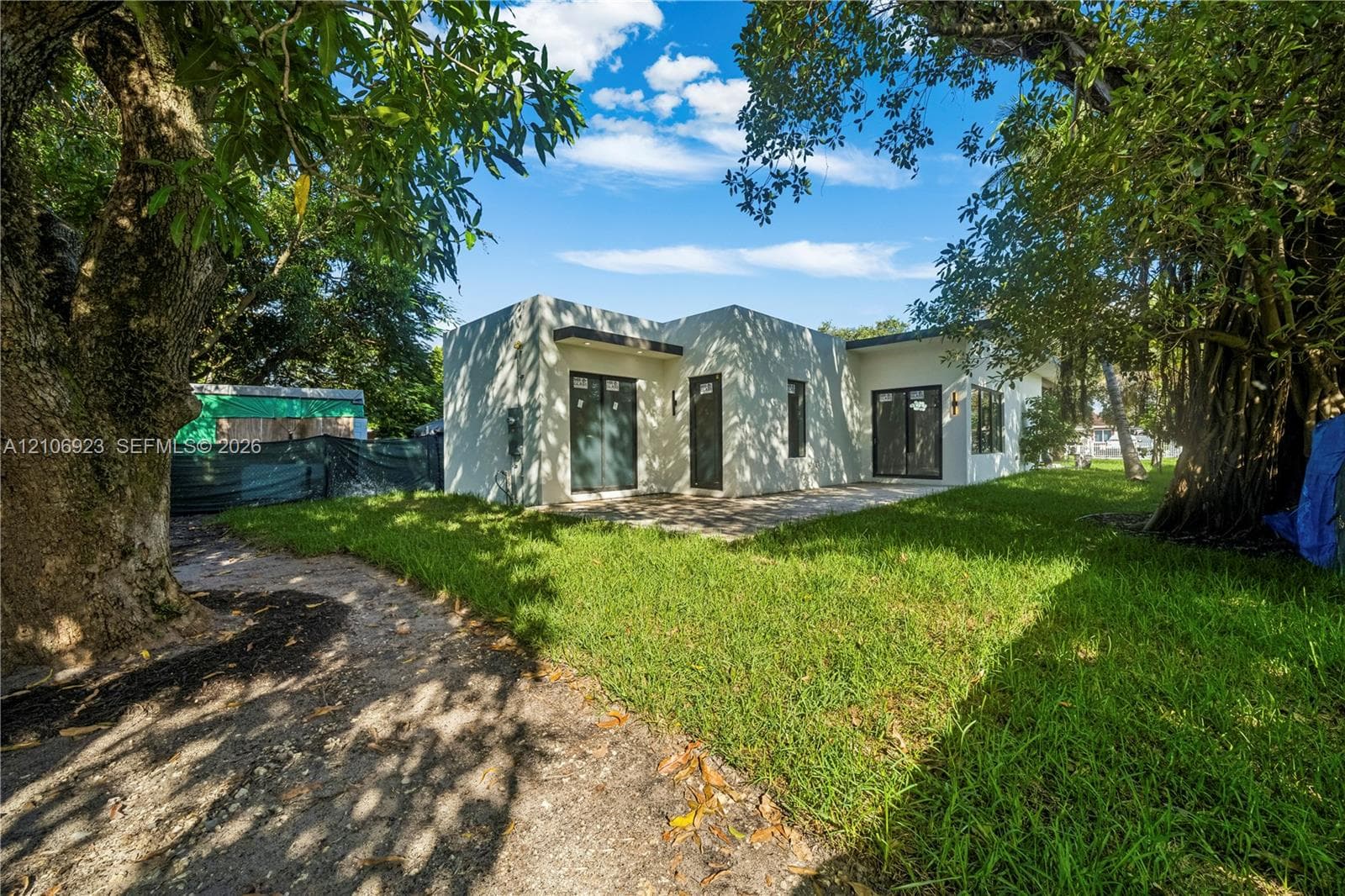 Stucco exterior residence featuring a flat roofline, glass sliding doors, dark-frame windows, and an expansive grass yard with mature trees