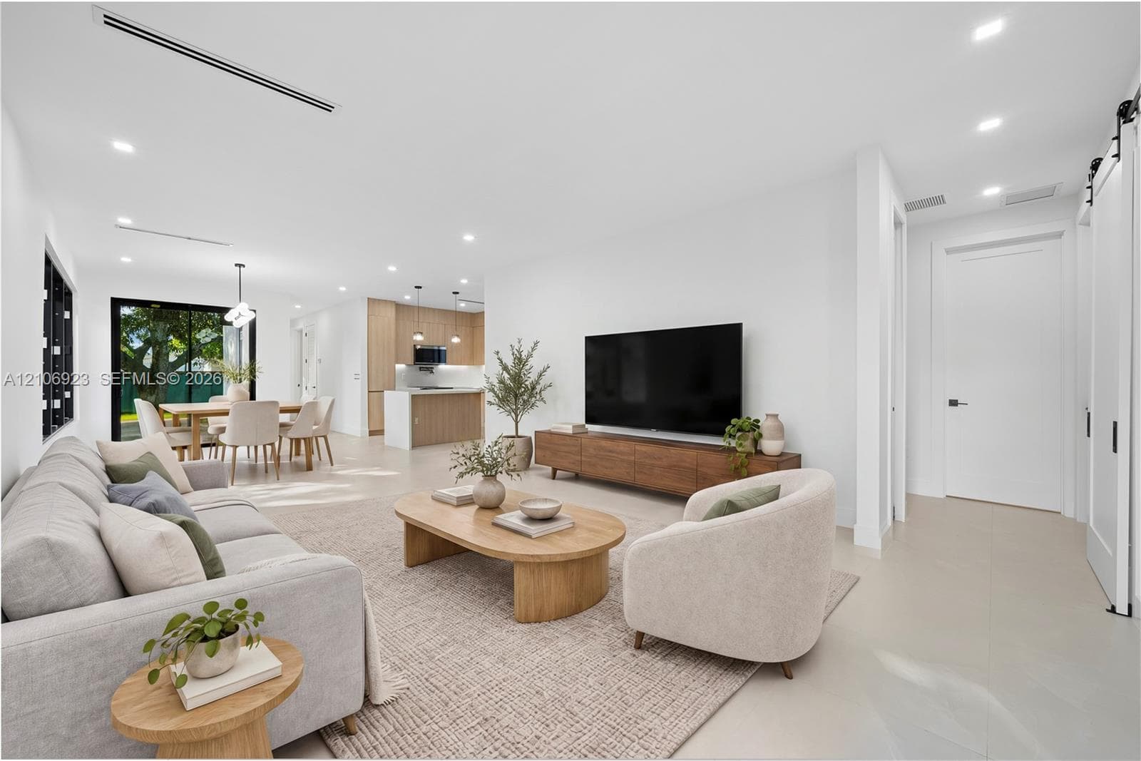 Open-concept interior featuring light-toned flooring, recessed lighting, linear HVAC diffusers, white sliding barn door, and kitchen cabinetry with wood-finish accents