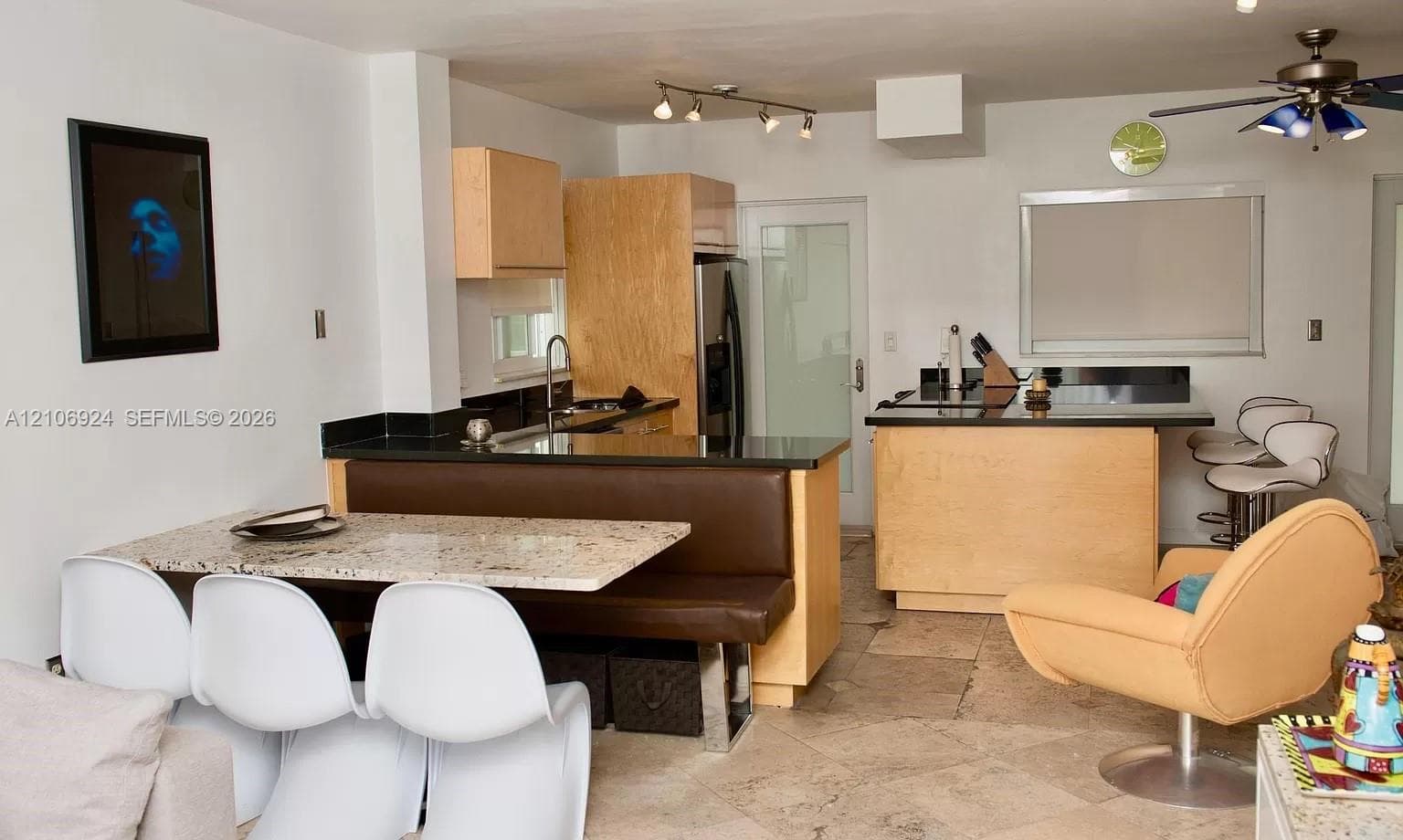 Kitchen featuring light-finish cabinetry, black stone countertops, a breakfast bar with built-in booth seating, stone flooring, and track lighting