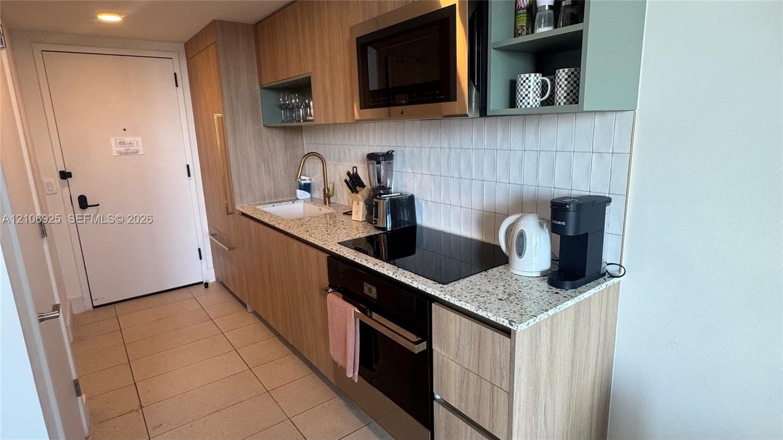 Stacked laundry unit housed in a dedicated closet with a white louvered door and tile flooring