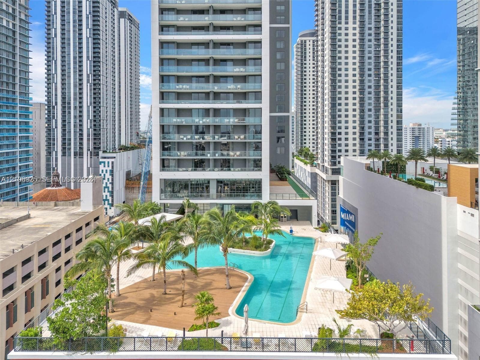 Elevated swimming pool featuring a lap lane, surrounding paved sundeck, integrated palm tree landscaping, and metal perimeter railing