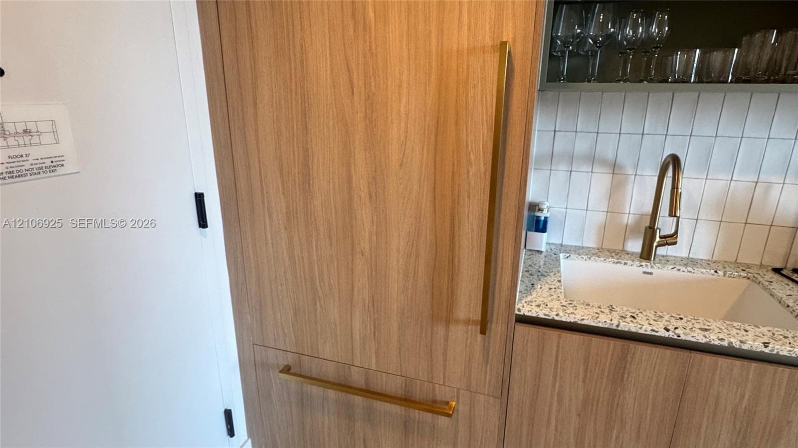 Bathroom featuring a wood-finish vanity with a stone-top vessel sink, matte gold faucet, geometric floor tile, and a glass-enclosed shower with vertical wall tile