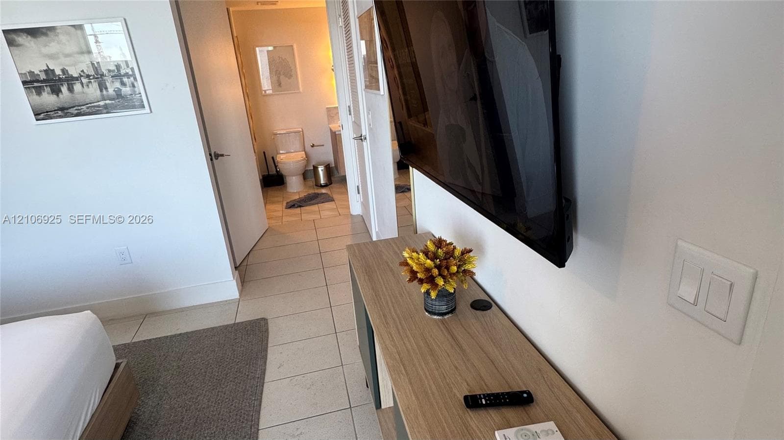 Wall-mounted flat-screen display, custom floating console with wood-finish cabinetry, and neutral tile flooring