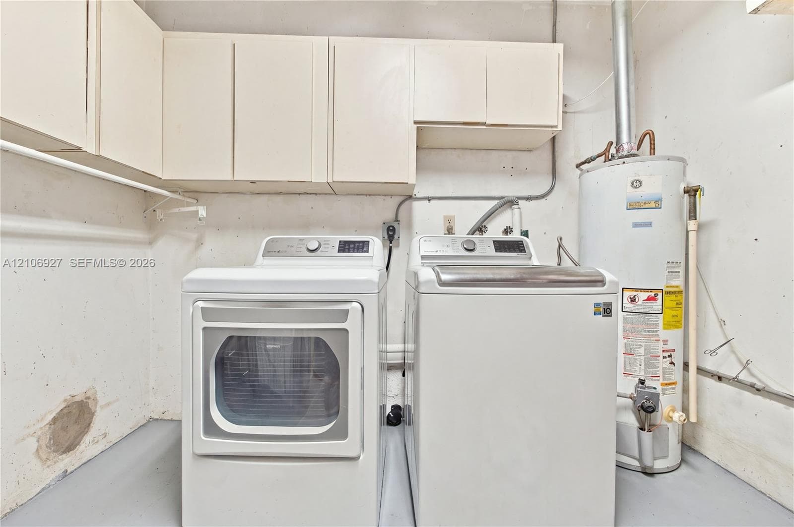 Utility space featuring white overhead cabinetry, dedicated washer and dryer connections, and a water heater