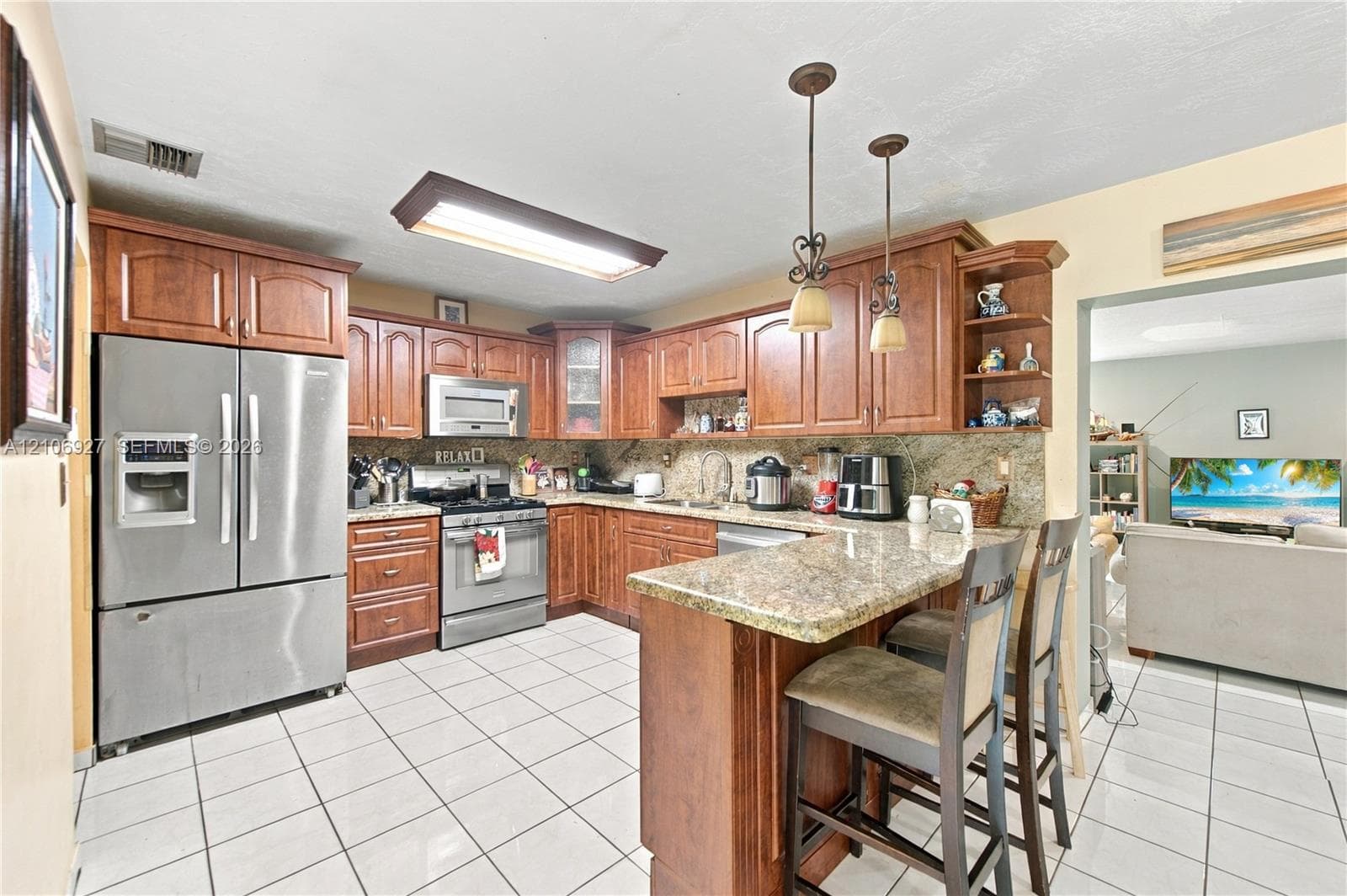 Kitchen featuring wood cabinetry, stone countertops, stainless steel appliances, ceramic tile flooring, and dual hanging pendant lights