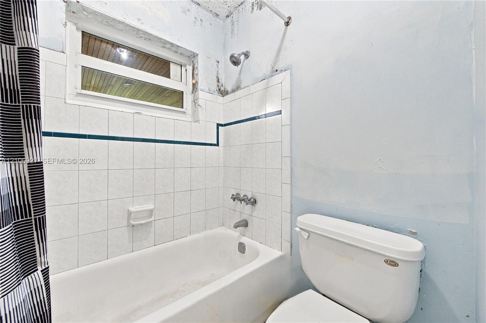 Bathroom featuring a porcelain tub, wall-mounted shower head, white tiled surround with decorative trim, and a horizontal window