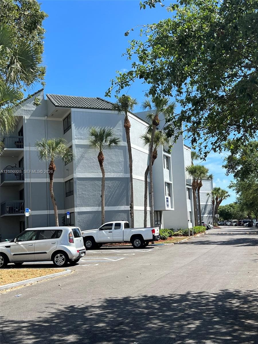 Multi-story exterior featuring a textured stucco facade, covered balconies, and mature palm trees