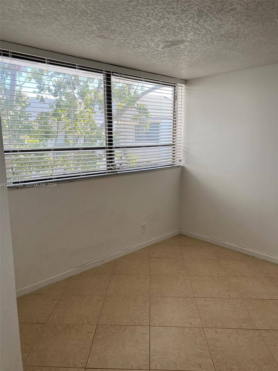 Expansive window featuring horizontal blinds, textured ceiling, and neutral ceramic tile flooring