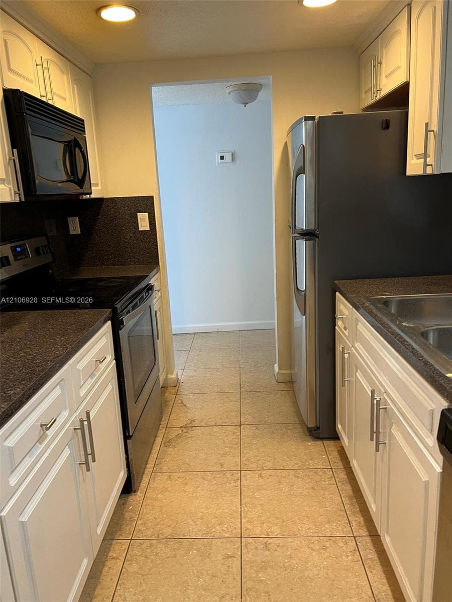 Kitchen featuring white cabinetry with brushed metal hardware, dark stone-finish countertops, stainless steel appliances, and tile flooring