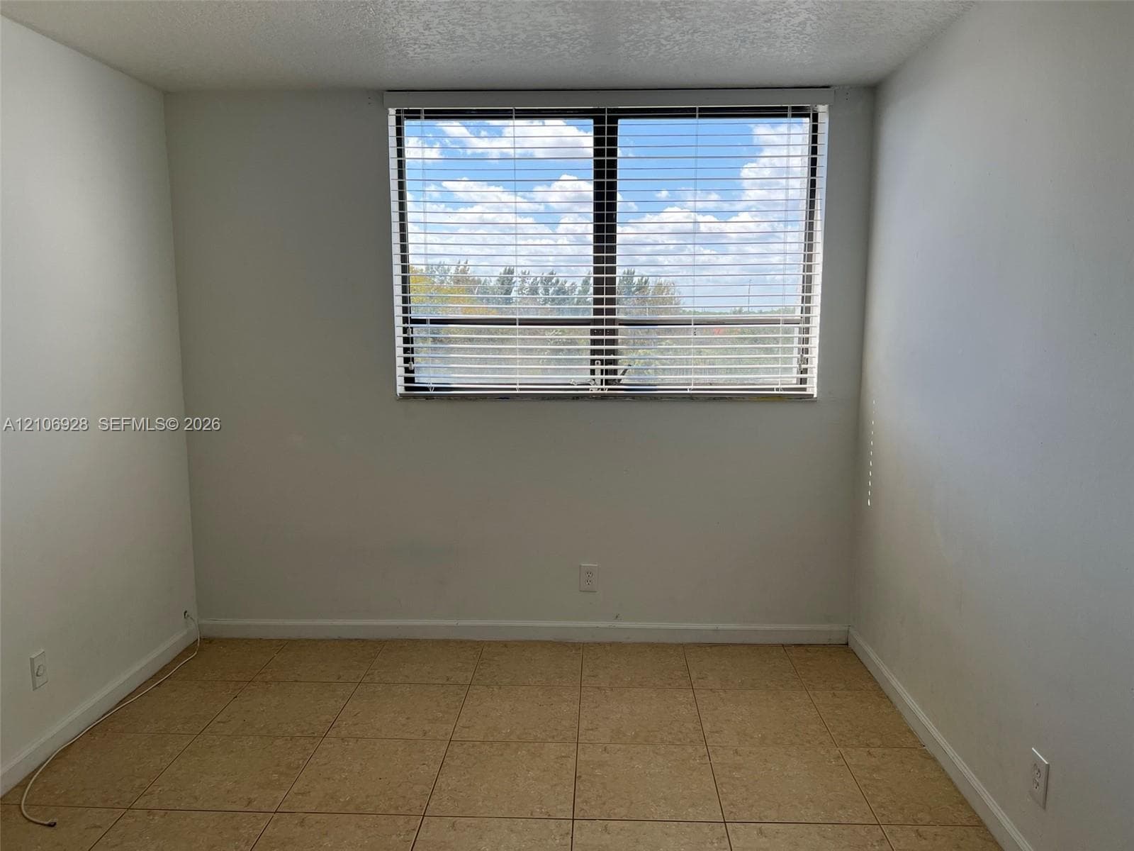 Room interior featuring neutral wall finishes, tile flooring, and a large window with horizontal blinds