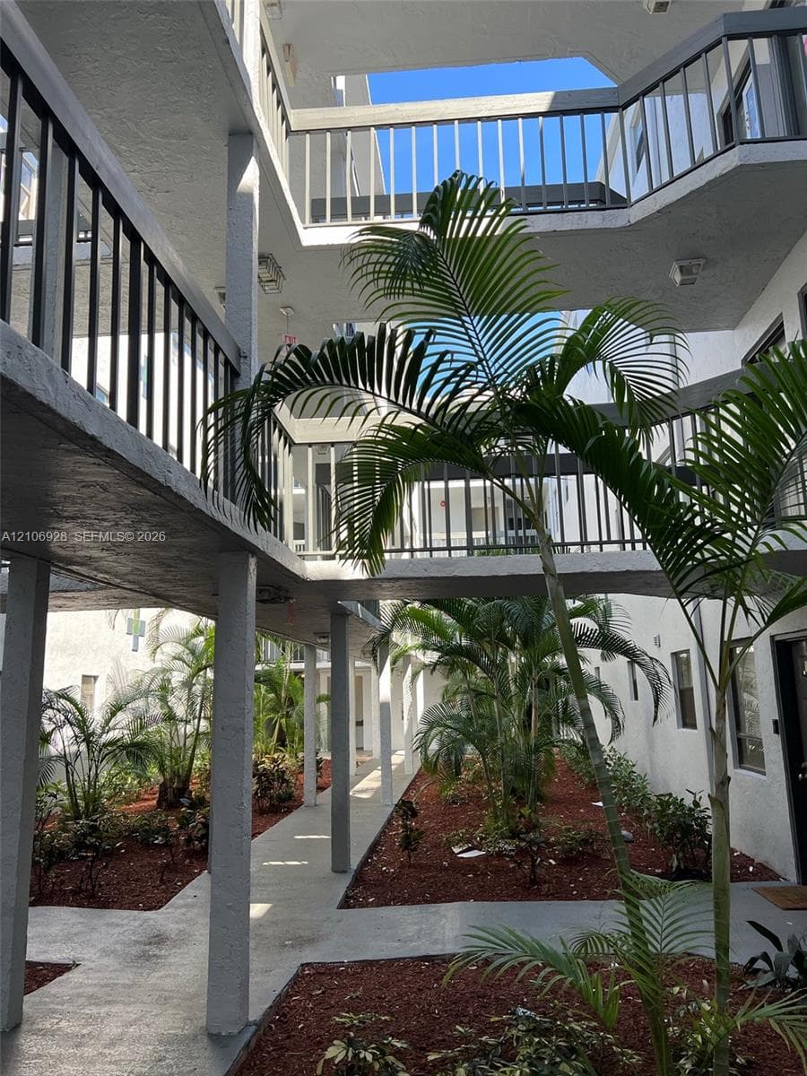 Open-air central courtyard featuring multi-level corridors, metal railing systems, covered concrete walkways, and landscaped planting beds with palm trees
