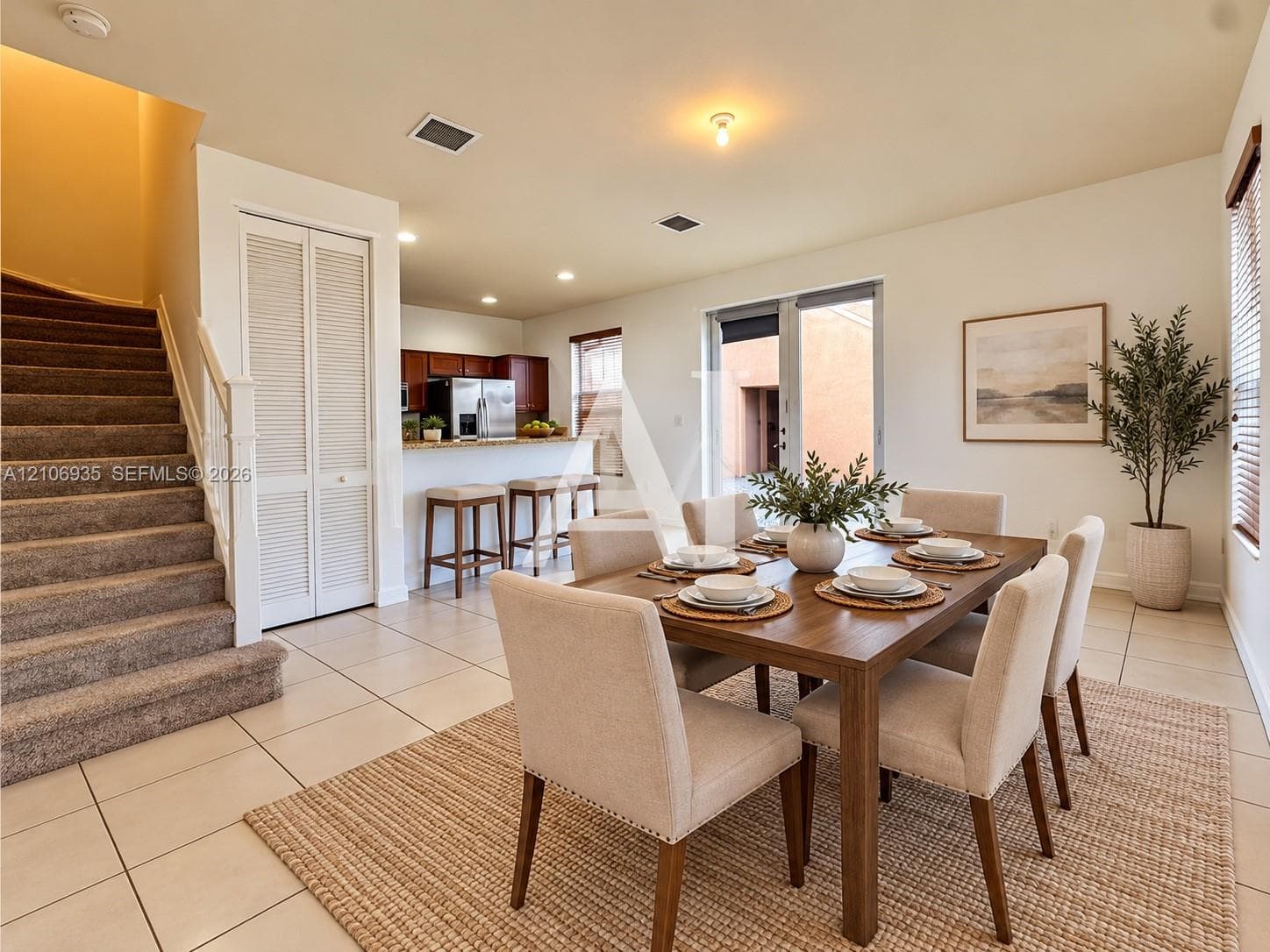 Open-concept floor plan featuring ceramic tile flooring, kitchen with peninsula breakfast bar, glass paneled exterior door, and carpeted staircase with white balusters