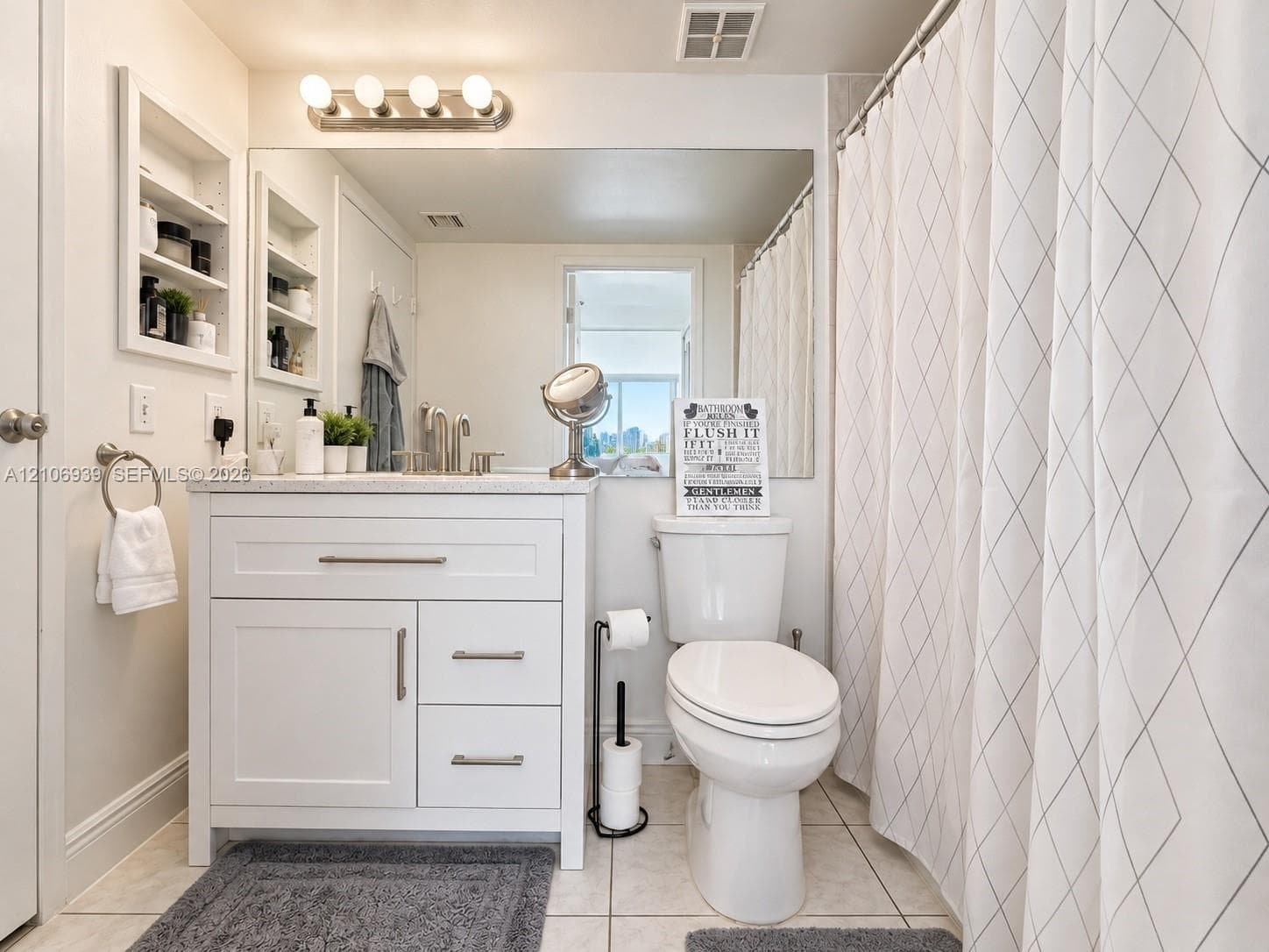 Bathroom featuring a white vanity cabinet with stone countertop, undermount sink, brushed nickel hardware, and built-in recessed wall shelving