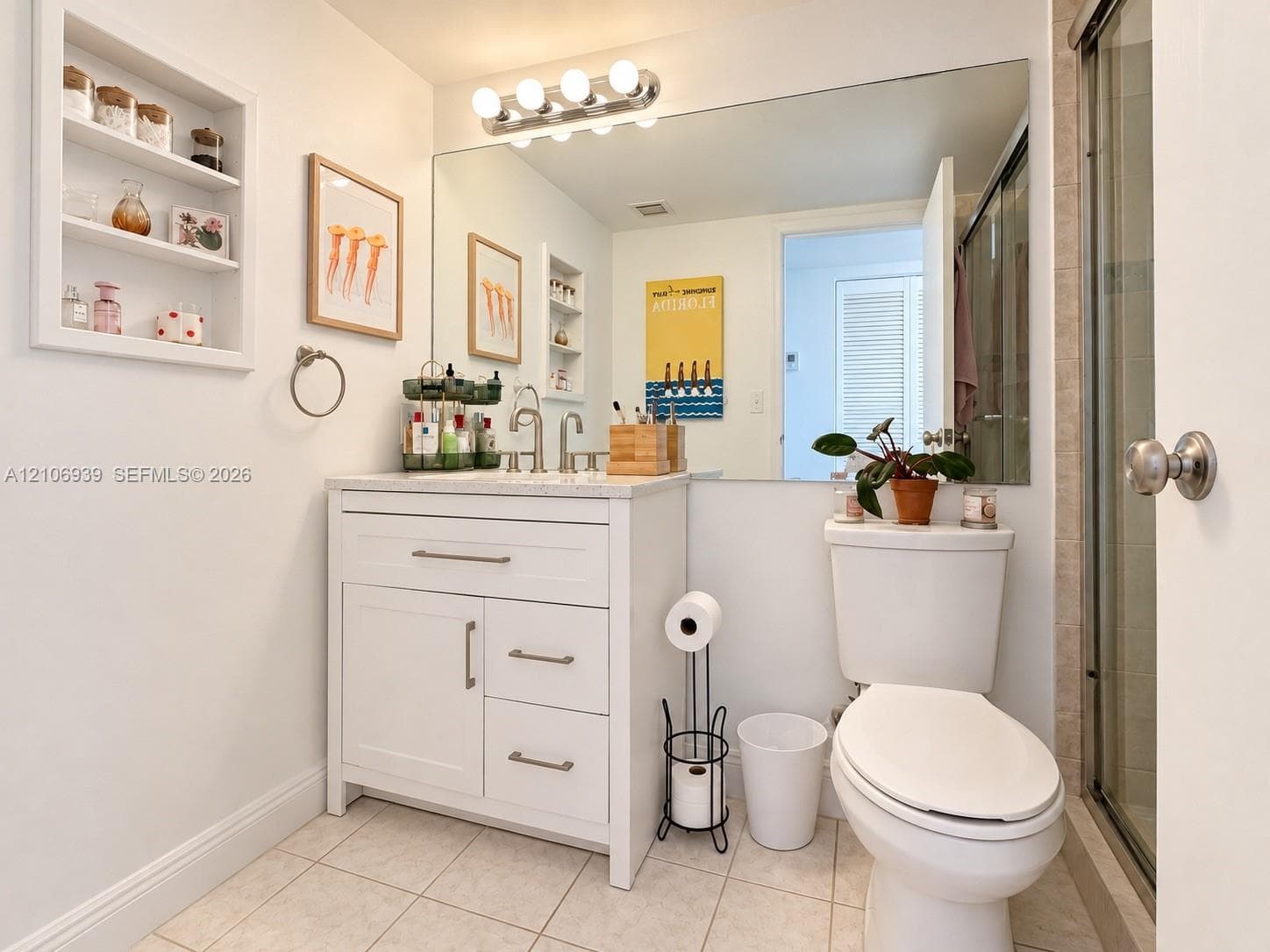 Bathroom featuring a vanity with shaker-style cabinetry, light-toned stone countertop, integrated shelving, large-format mirror, and glass-enclosed shower