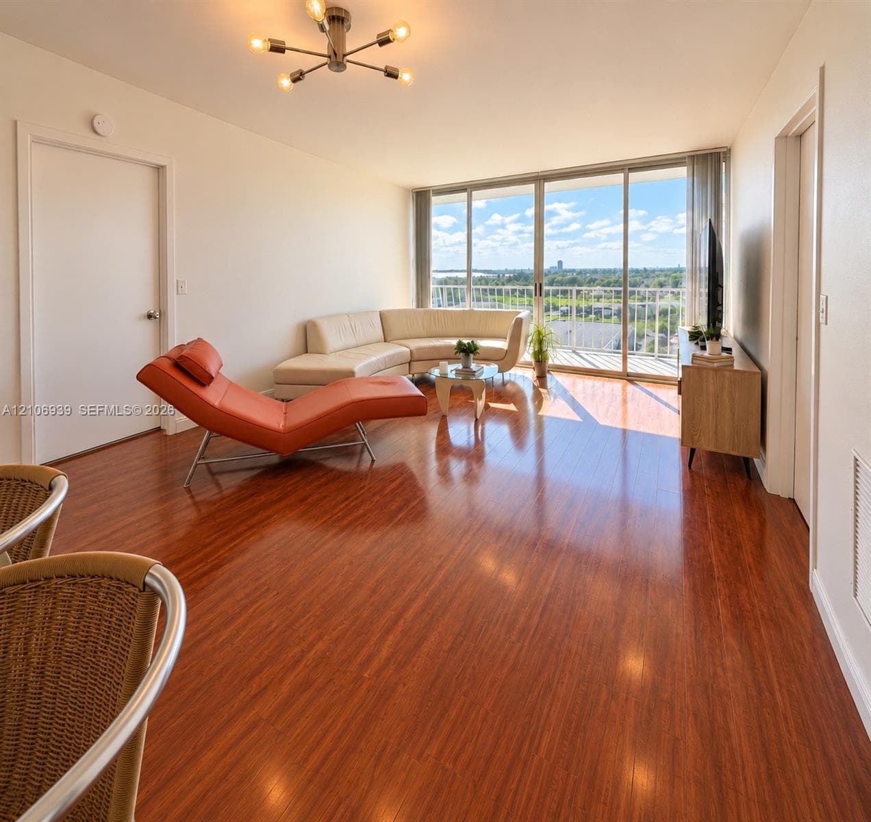 Living area featuring wood-finish flooring, floor-to-ceiling sliding glass doors, a balcony, and a multi-arm modern light fixture