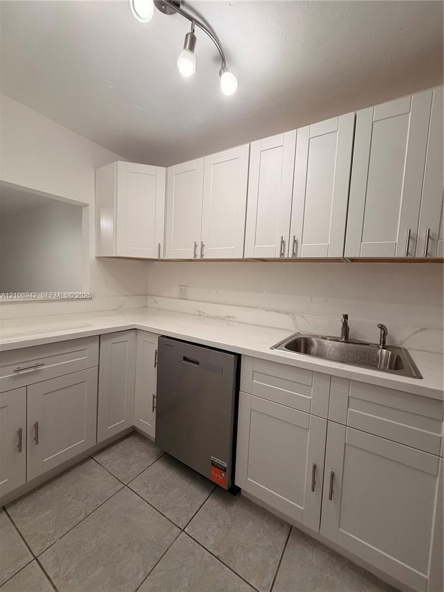 White shaker-style cabinetry, stone-finish countertops with integrated backsplash, stainless steel dishwasher, stainless steel sink with dual-handle faucet, and ceramic tile flooring