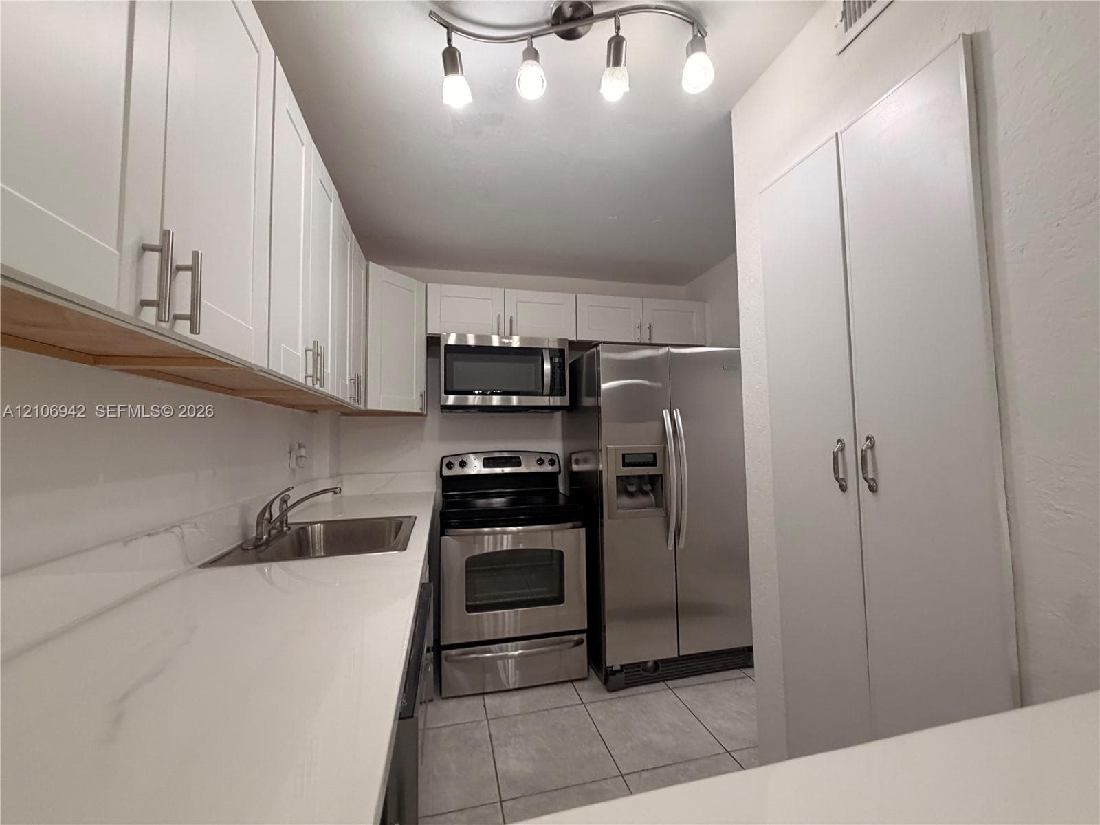 Kitchen featuring white shaker-style cabinetry, solid-surface countertops, stainless steel appliances, tile flooring, and multi-bulb track lighting