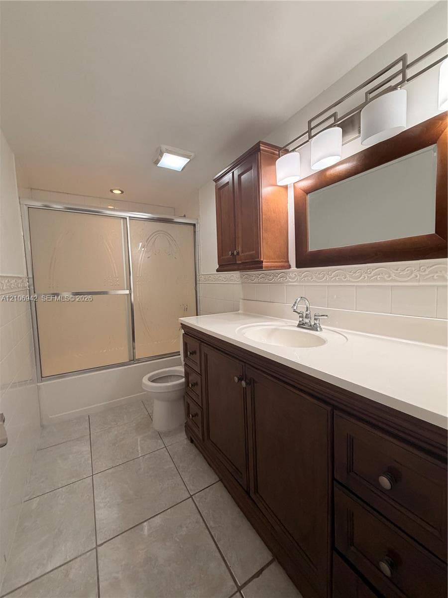 Bathroom featuring a vanity with wood-finish cabinetry, a white countertop with an integrated basin, a coordinating wood-framed mirror, a multi-light fixture, and a sliding glass shower door