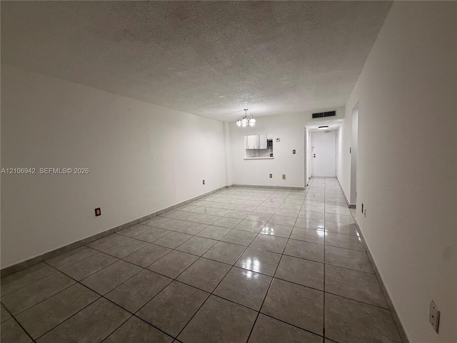Open interior space featuring light-toned tile flooring, a pass-through window to an additional area, and a ceiling-mounted light fixture