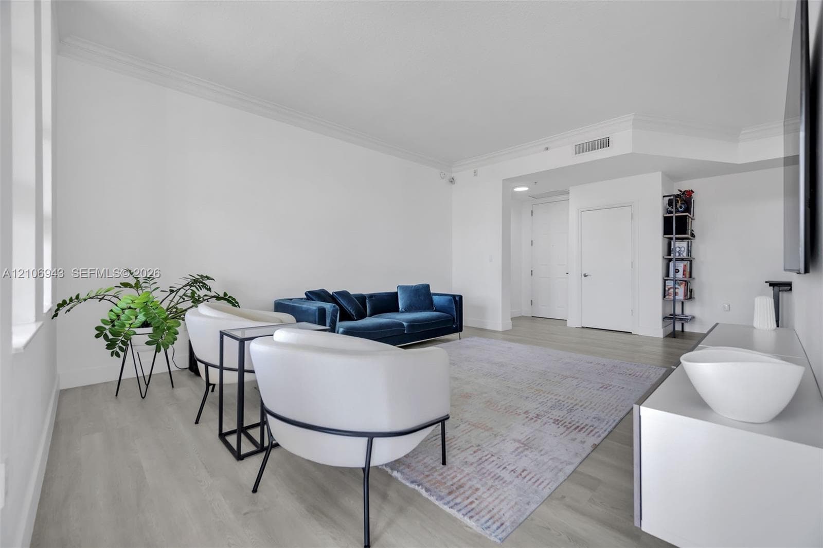 Open-concept living space featuring wood-finish flooring, crisp neutral wall paint, crown molding, and tall vertical windows