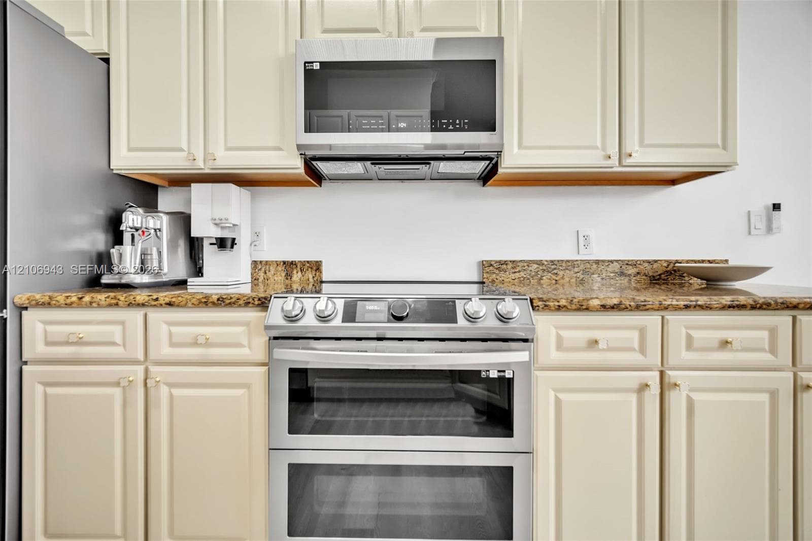 Kitchen featuring cream-toned raised-panel cabinetry, stone countertops, double oven stainless steel range, and a mounted stainless steel microwave