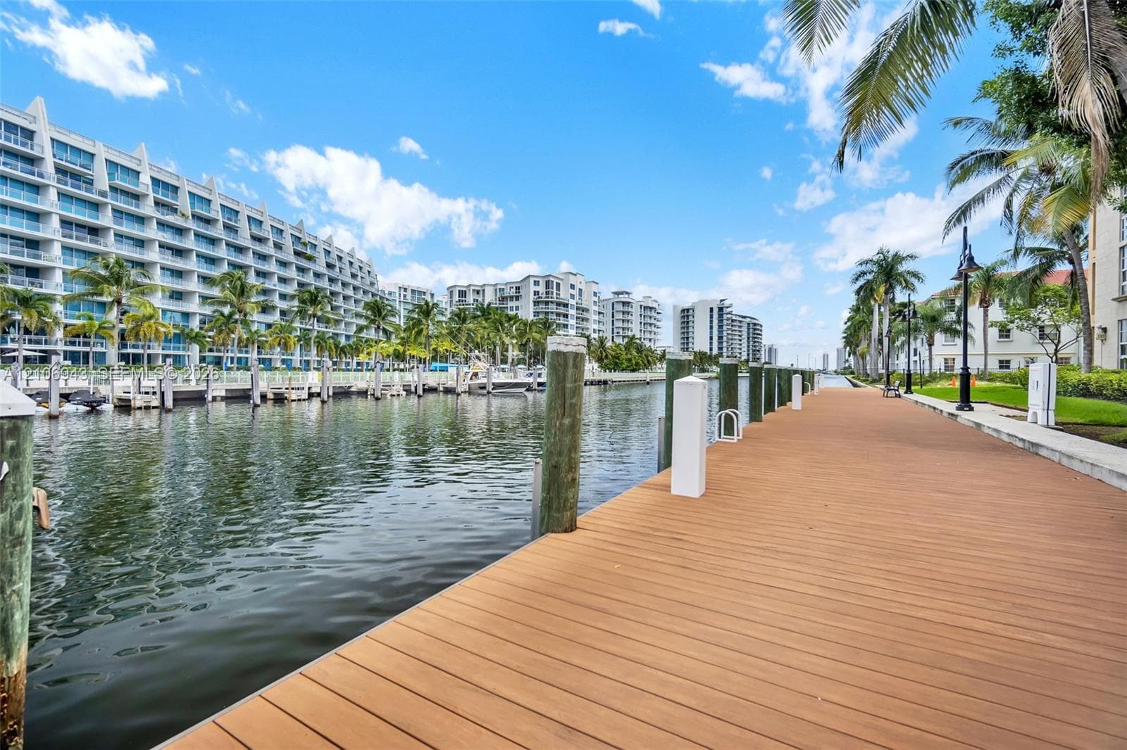 Waterfront boardwalk featuring a wood-finish deck, vertical wood pilings, and lamp post lighting