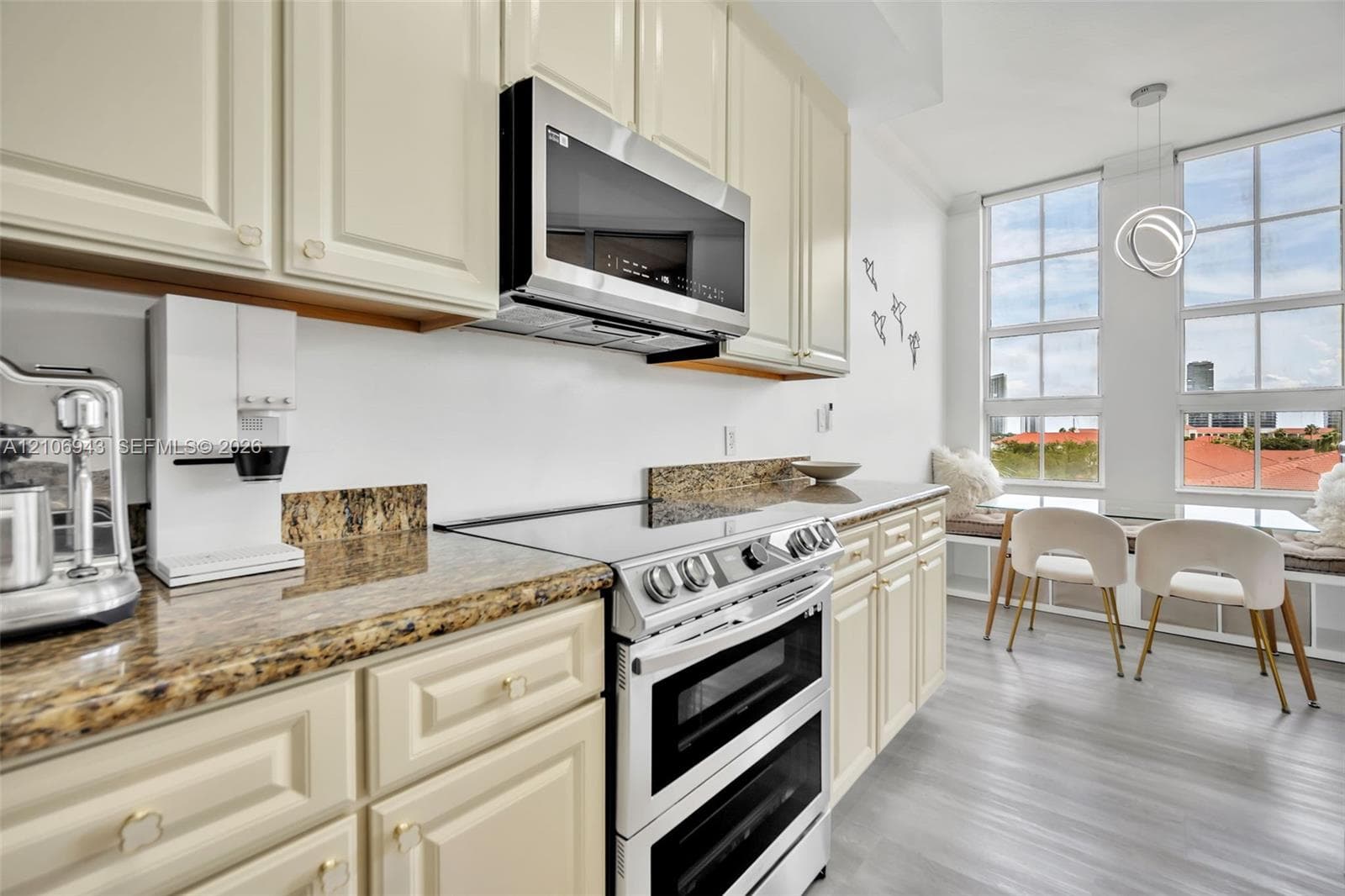 Kitchen featuring cream-colored cabinetry, stone countertops, stainless steel dual-oven range, built-in microwave, and large grid-pane windows