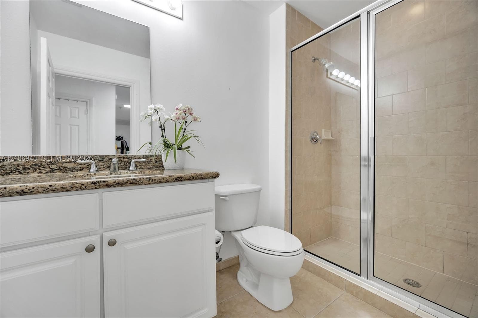 Bathroom featuring a vanity with white cabinetry, a stone-finish countertop, an integrated sink with a chrome faucet, a walk-in shower with glass enclosure, and tiled flooring