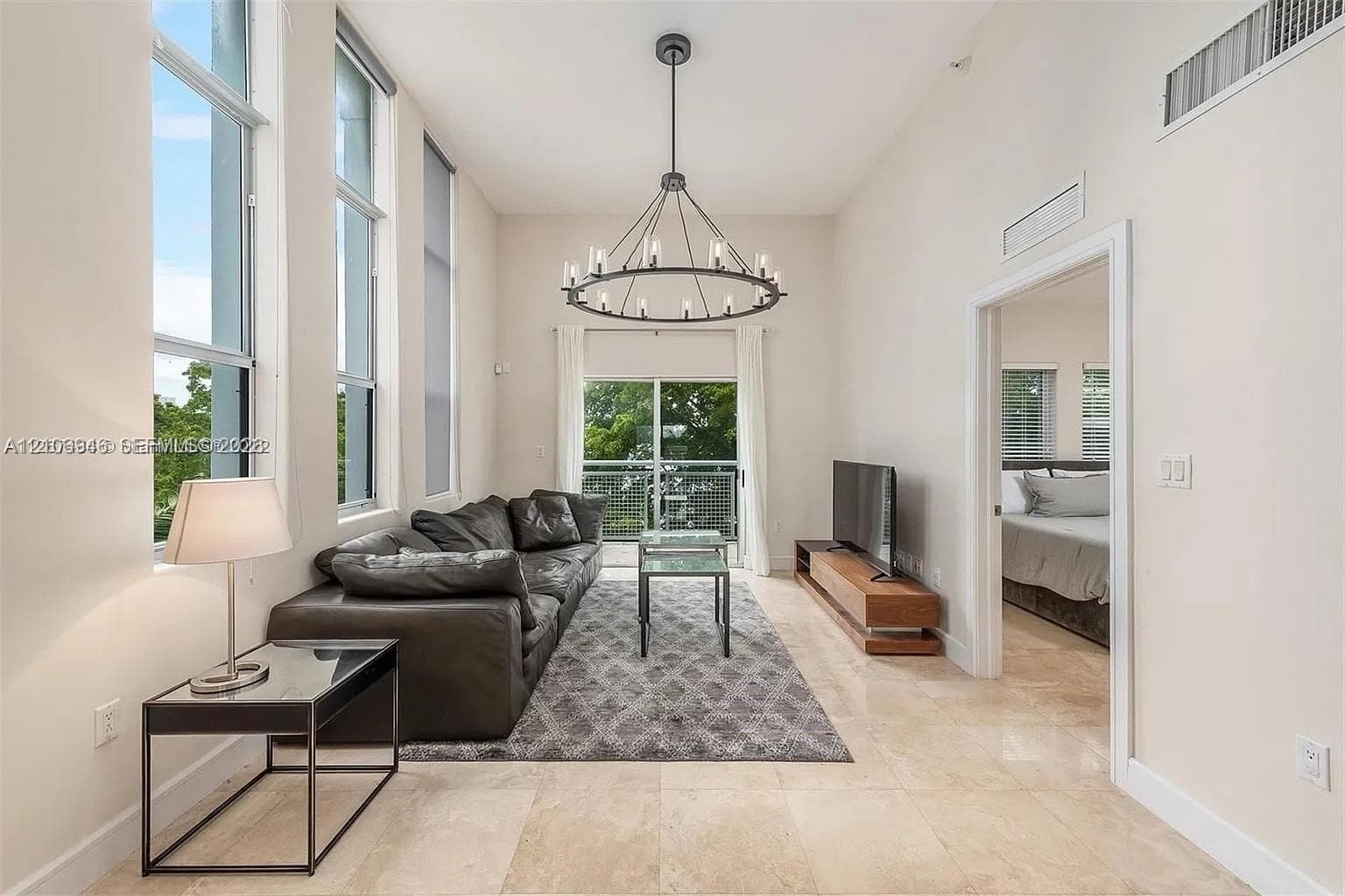 High ceilings with floor-to-ceiling windows, polished stone flooring, and a decorative circular chandelier