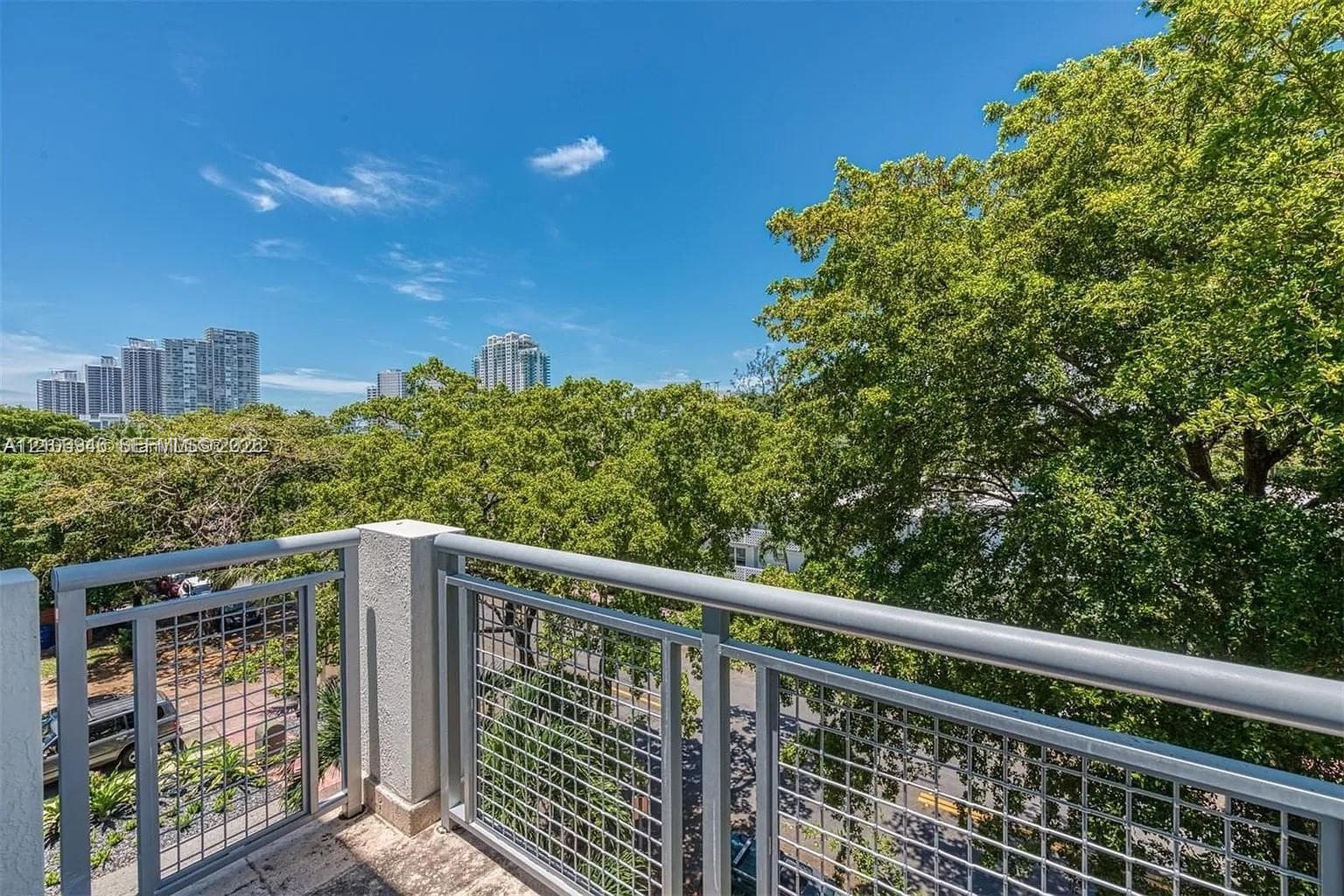 Private balcony with metal mesh railings, concrete flooring, and mature canopy trees