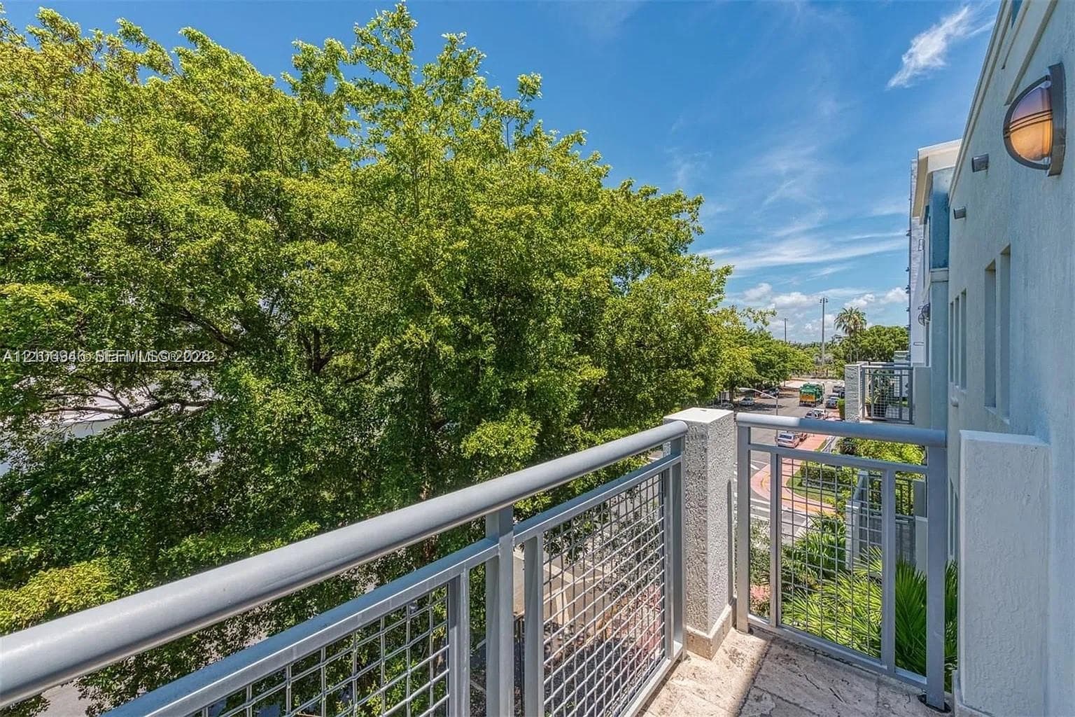 Exterior balcony featuring metal railings with grid-patterned panels, stone flooring, and wall-mounted exterior lighting